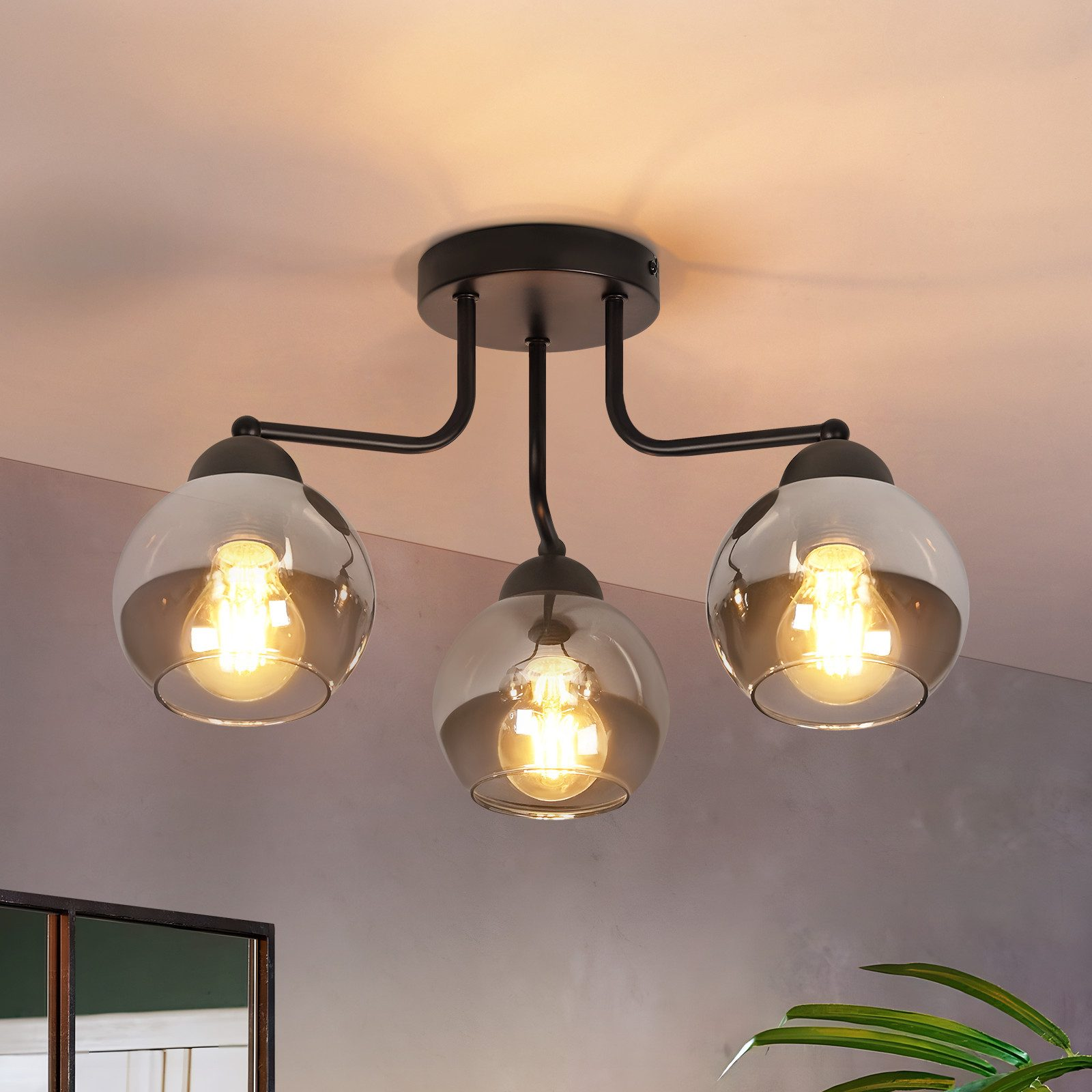 Una plafoniera con tre paralumi in vetro. Ogni paralume ha una lampadina. L'apparecchio è nero e il soffitto bianco.