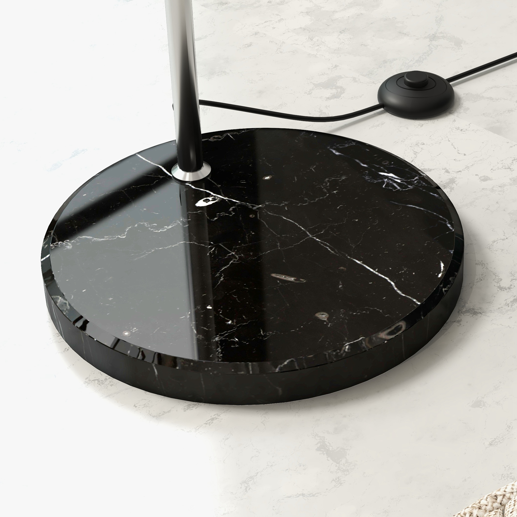 Una base per lampada in marmo nero con un palo cromato. Un cavo di alimentazione nero e un interruttore a pedale su una superficie bianca marmorizzata.