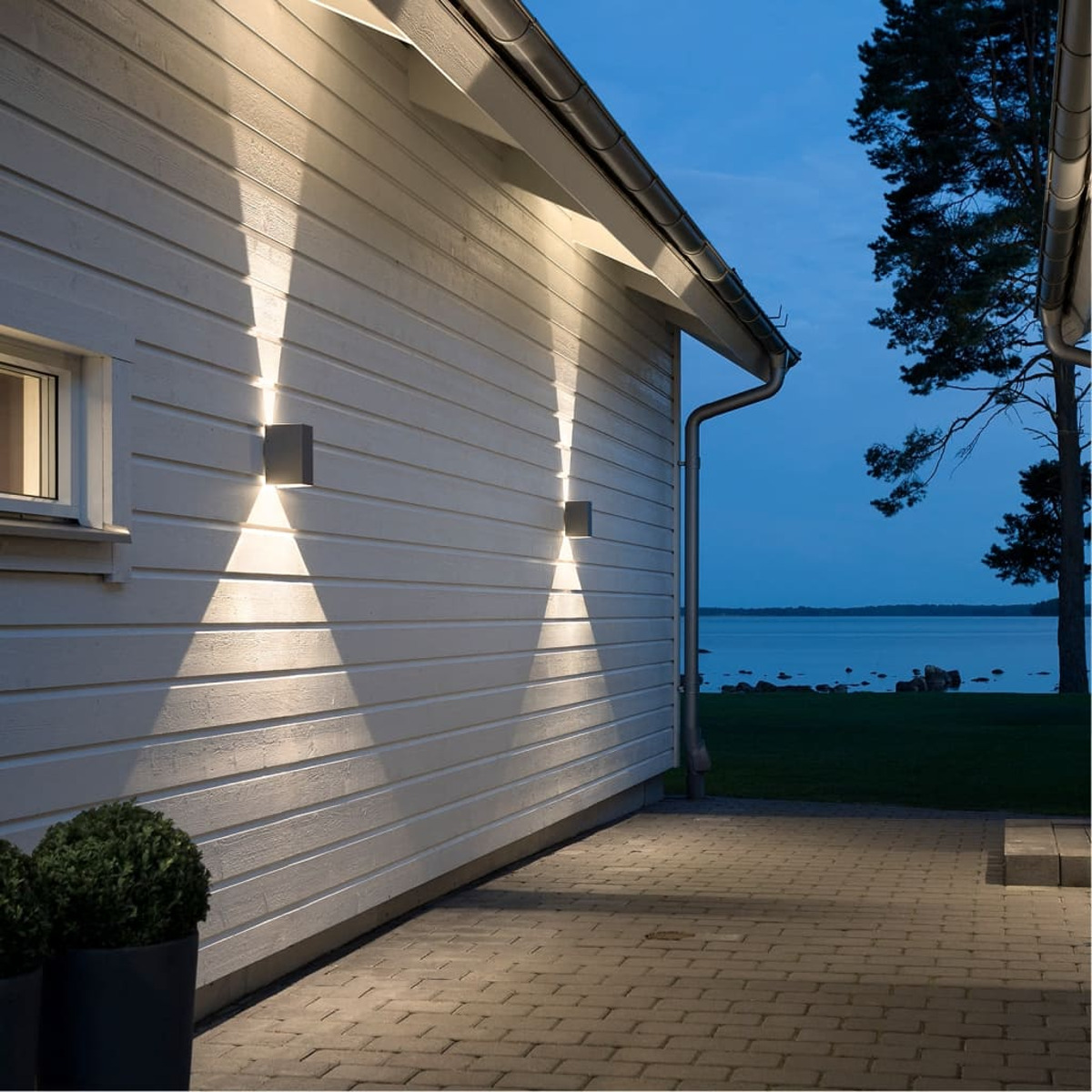 Scatto esterno di una casa bianca con due luci che illuminano il muro. Un patio pavimentato conduce all'acqua.