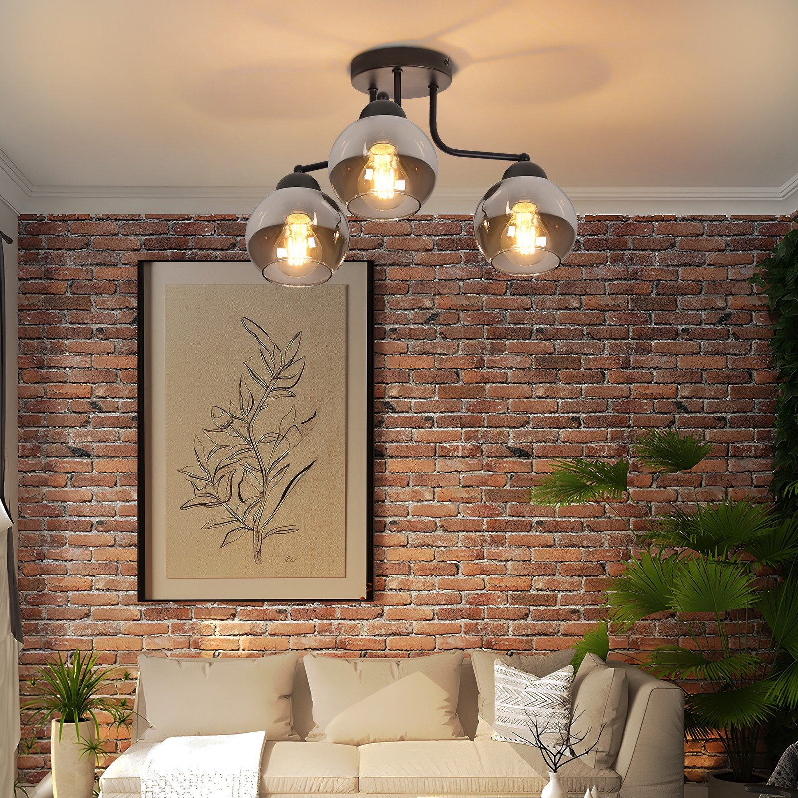 Una stanza con un muro di mattoni. Sono visibili un divano, un quadro incorniciato e un lampadario a tre lampadine. Sono presenti anche delle piante.