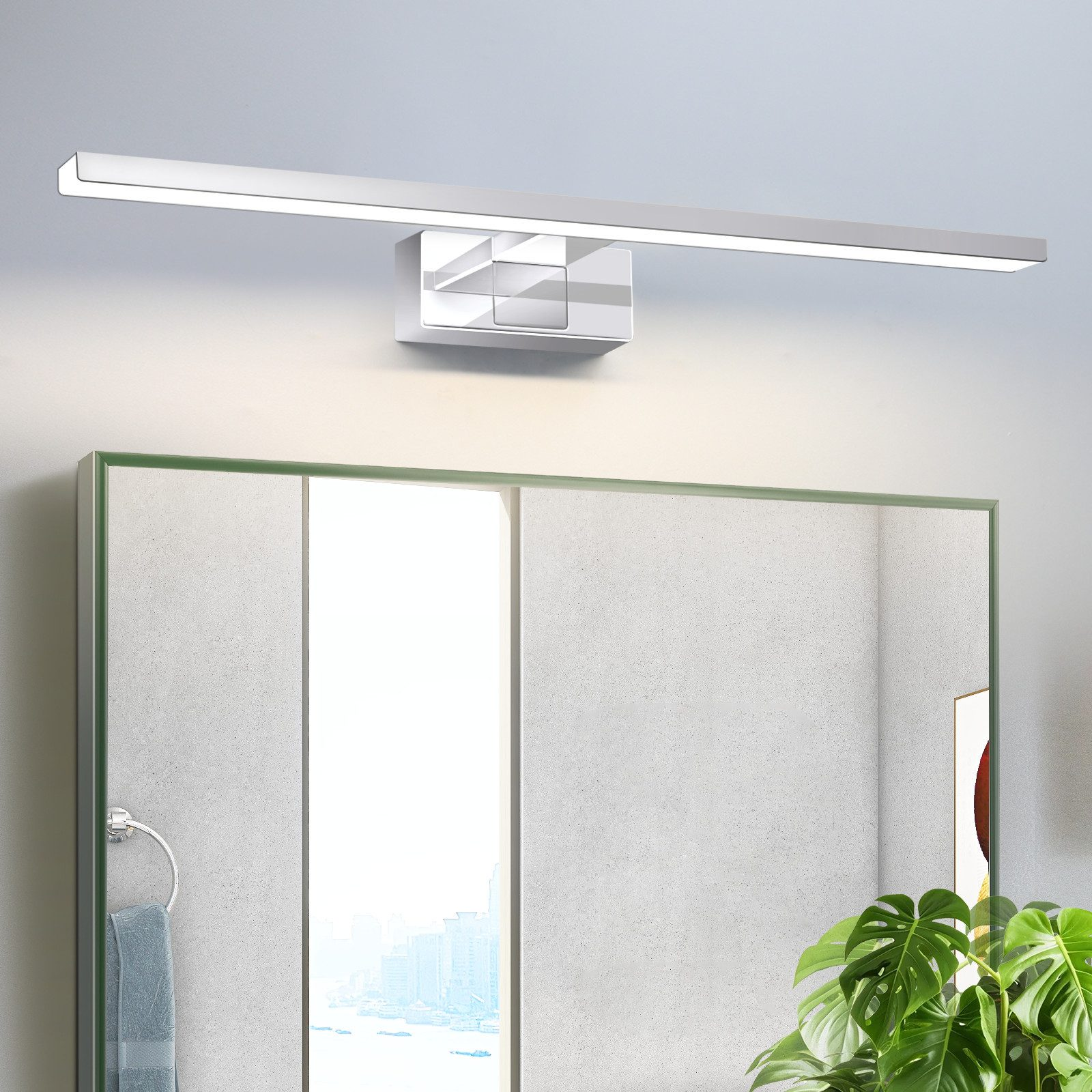 Un bagno con specchio, lampada e piante. Un asciugamano è appeso a un anello portasciugamani. Vista della città riflessa nello specchio.