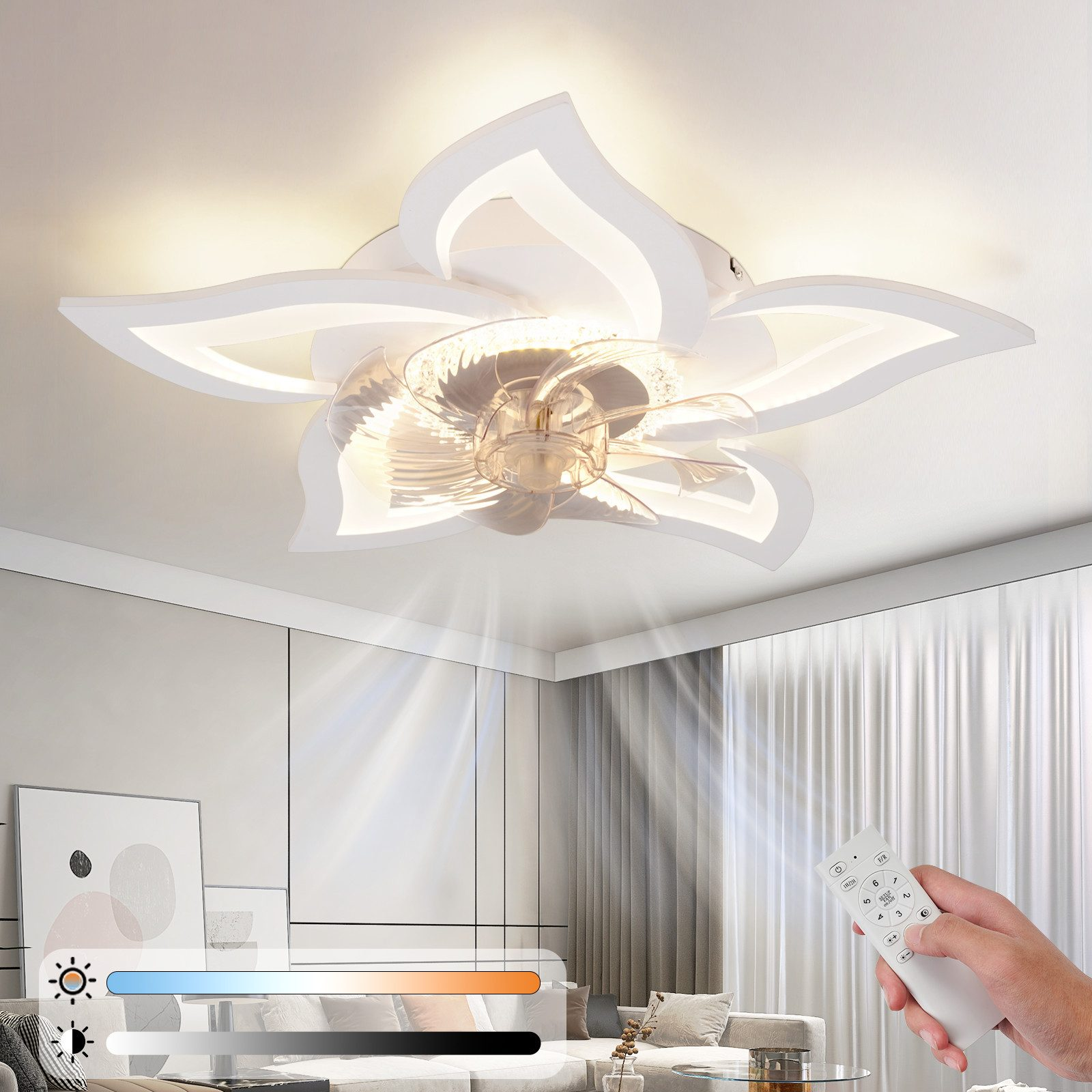 Un ventilatore da soffitto bianco a forma di fiore con luci è acceso. Una mano tiene un telecomando. La stanza ha tende, un divano e arte.