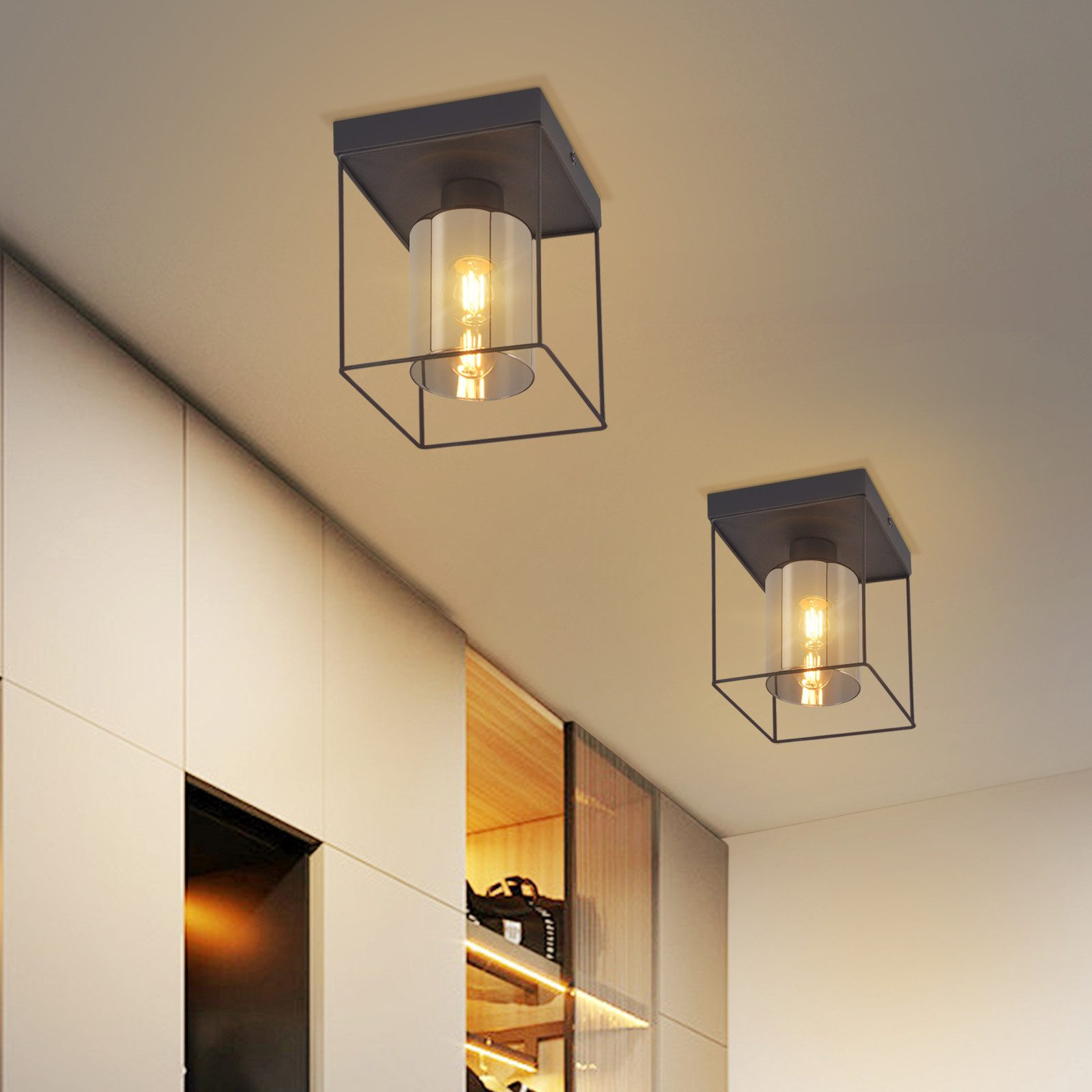 Due plafoniere con design a gabbia nera. Ognuna ha un cilindro di vetro attorno a una lampadina. Sotto ci sono degli armadi.