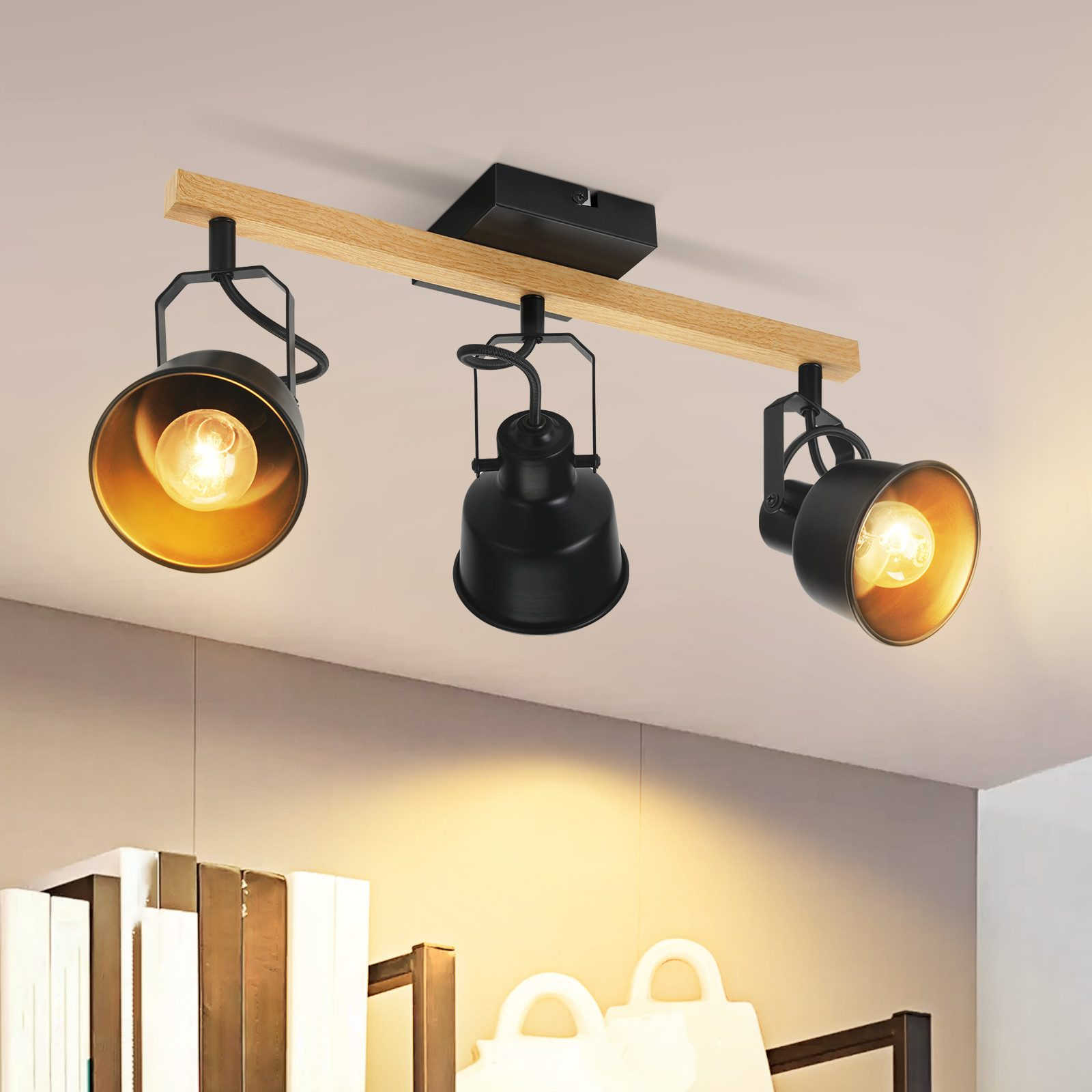 Tre faretti neri con interni dorati sono montati su una trave di legno. Le luci sono accese. Lo sfondo mostra una mensola e un soffitto bianco.