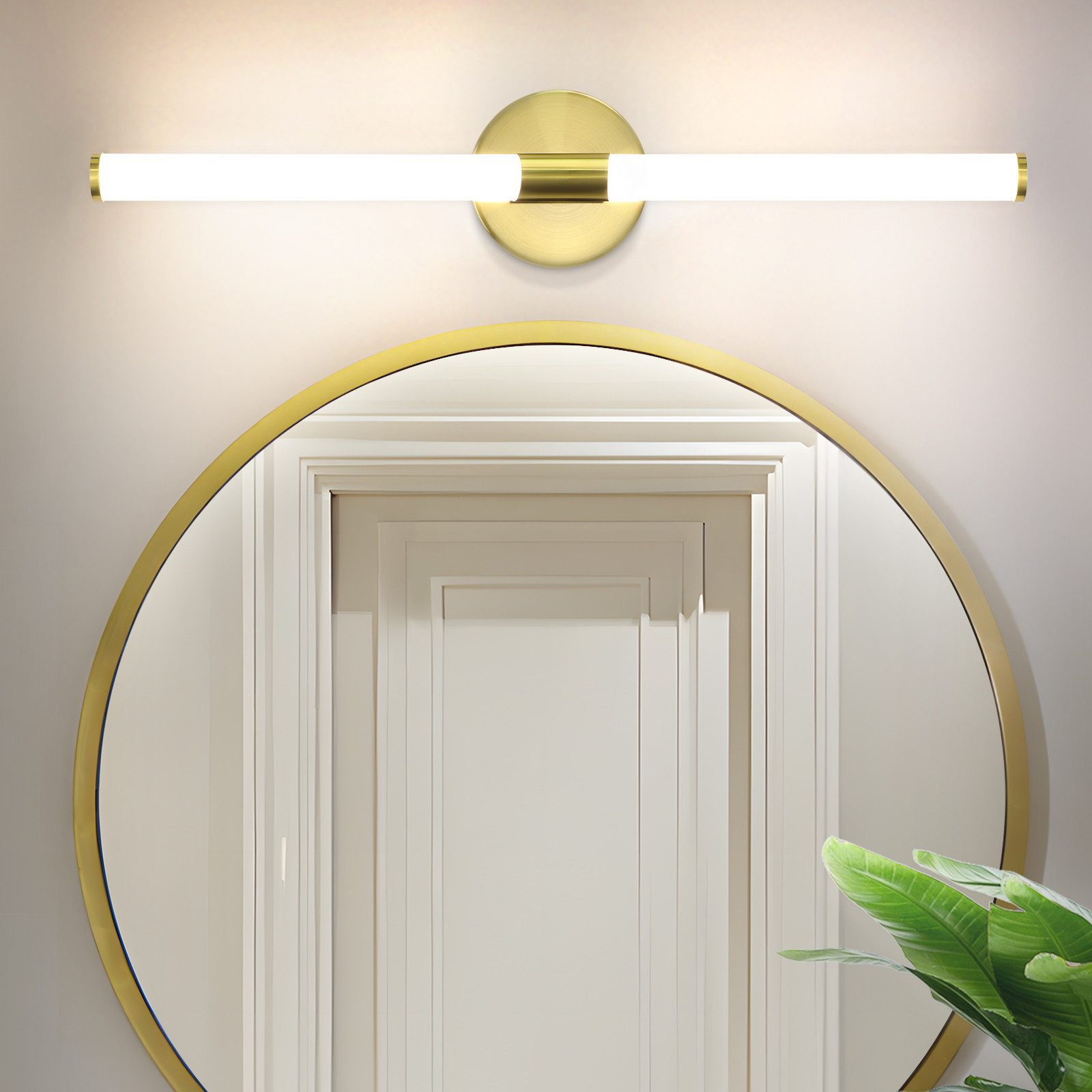 Uno specchio con cornice dorata con riflesso di porta bianca, un apparecchio di illuminazione dorato e foglie verdi.