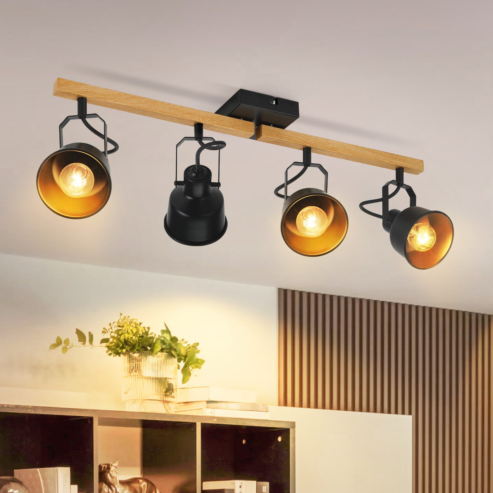 Lampa sufitowa z czterema czarnymi reflektorami. Oprawa jest przymocowana do drewnianej belki. W tle wazon z roślinami.