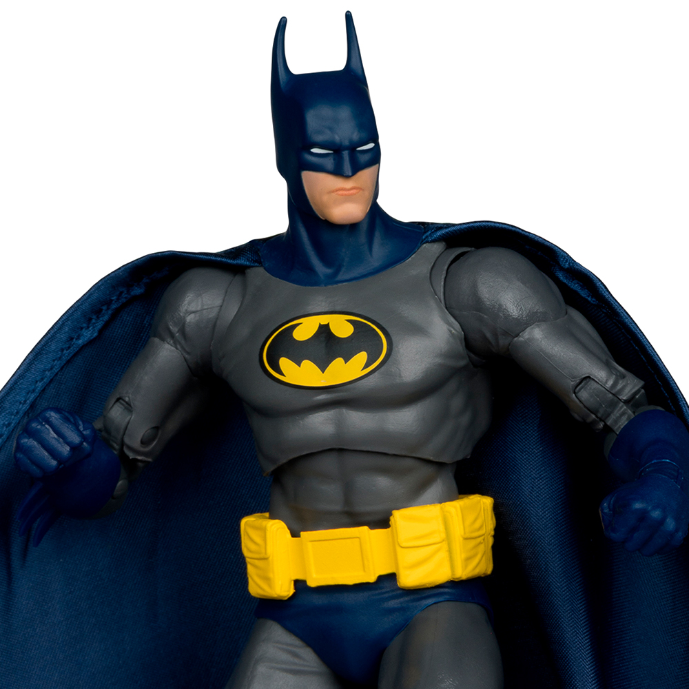 Action figure di Batman in costume grigio e blu, cintura gialla e simbolo del pipistrello. Mantello blu scuro. Sfondo bianco.