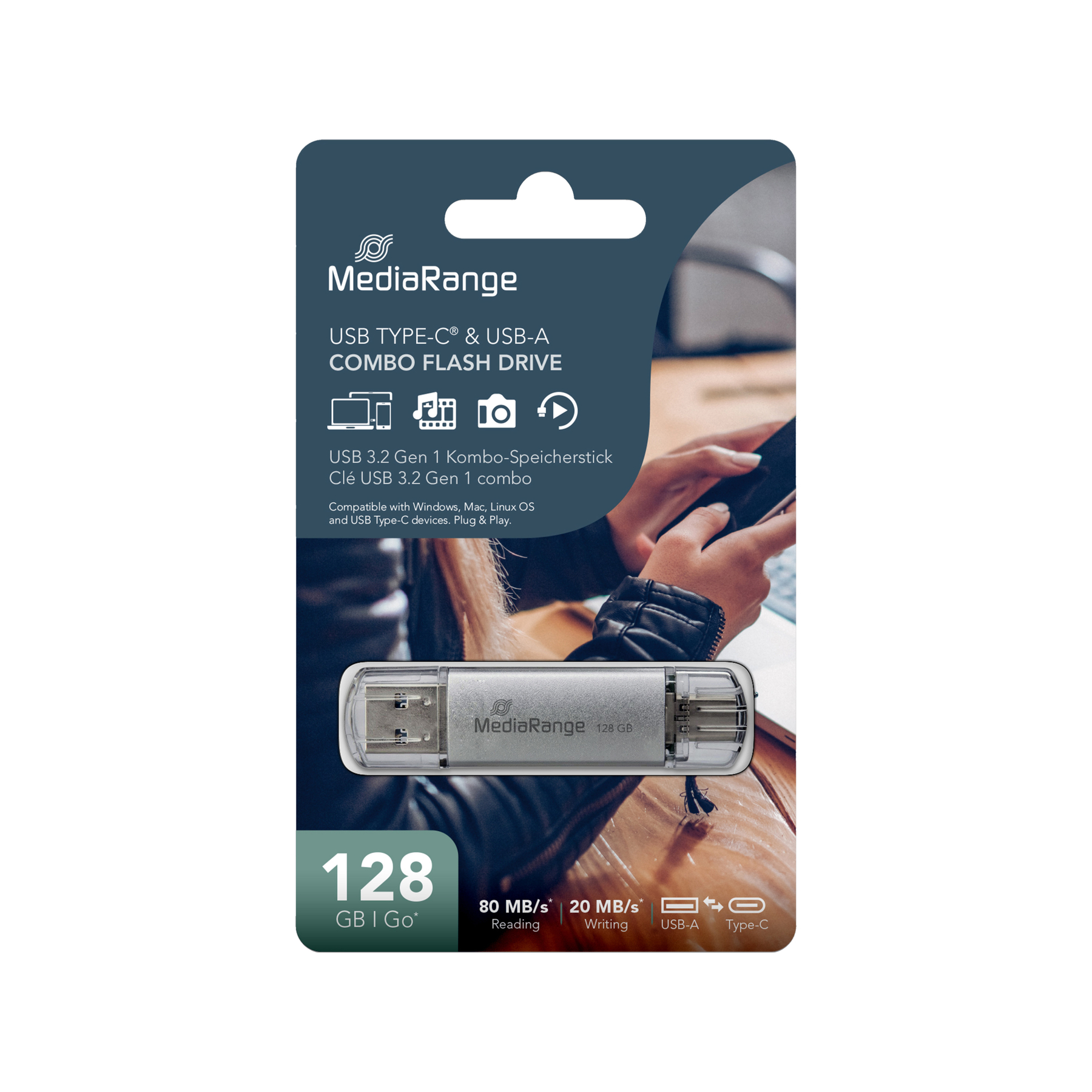 Srebrny pendrive USB MediaRange, 128 GB, w ciemnoniebieskim opakowaniu. Dłonie trzymające telefon w tle.