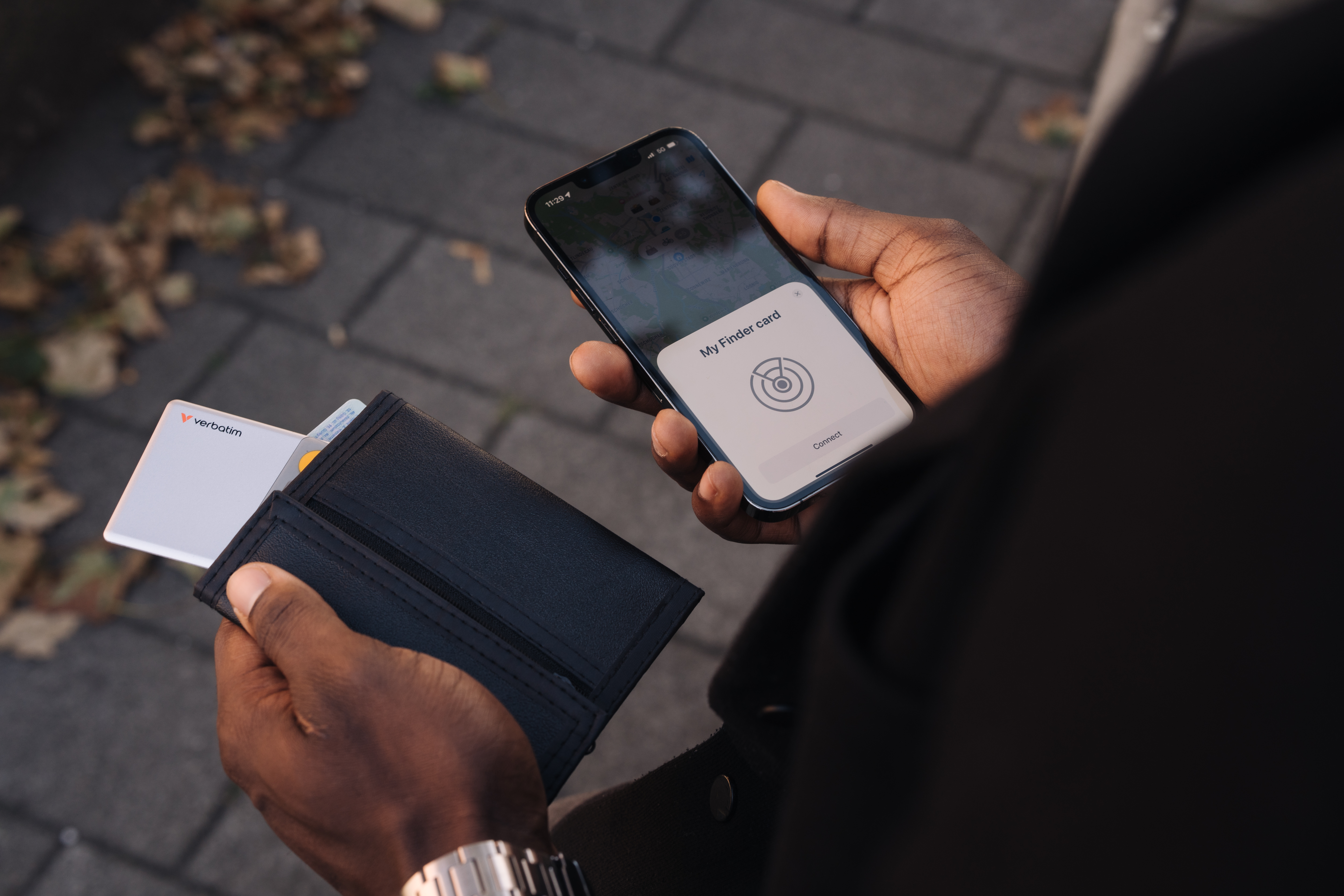 Una persona tiene in mano un telefono con 'My Finder card' e un portafoglio con una carta. Lo sfondo mostra foglie e una strada.
