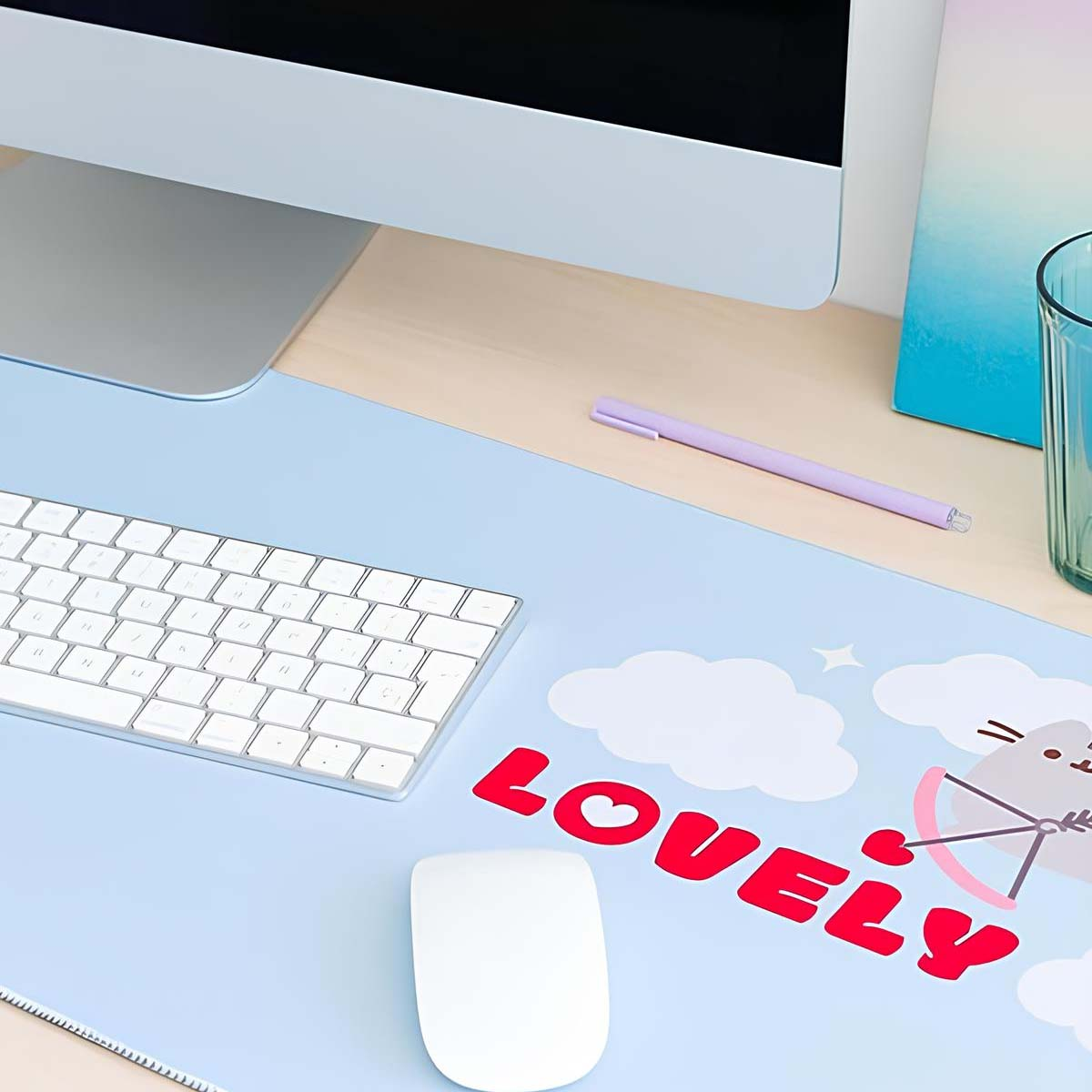 Un'impostazione scrivania con tastiera, mouse e un tappetino blu con 'LOVELY'. Sono presenti anche un monitor e una penna.
