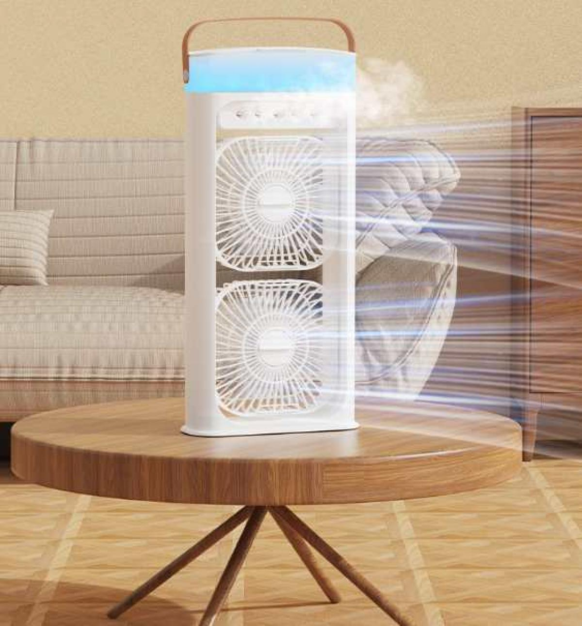 Ein weißer Luftkühler auf einem Holztisch. Zwei Ventilatoren im Inneren sichtbar. Im Hintergrund eine Couch und Möbel. Luft strömt aus dem Kühler.