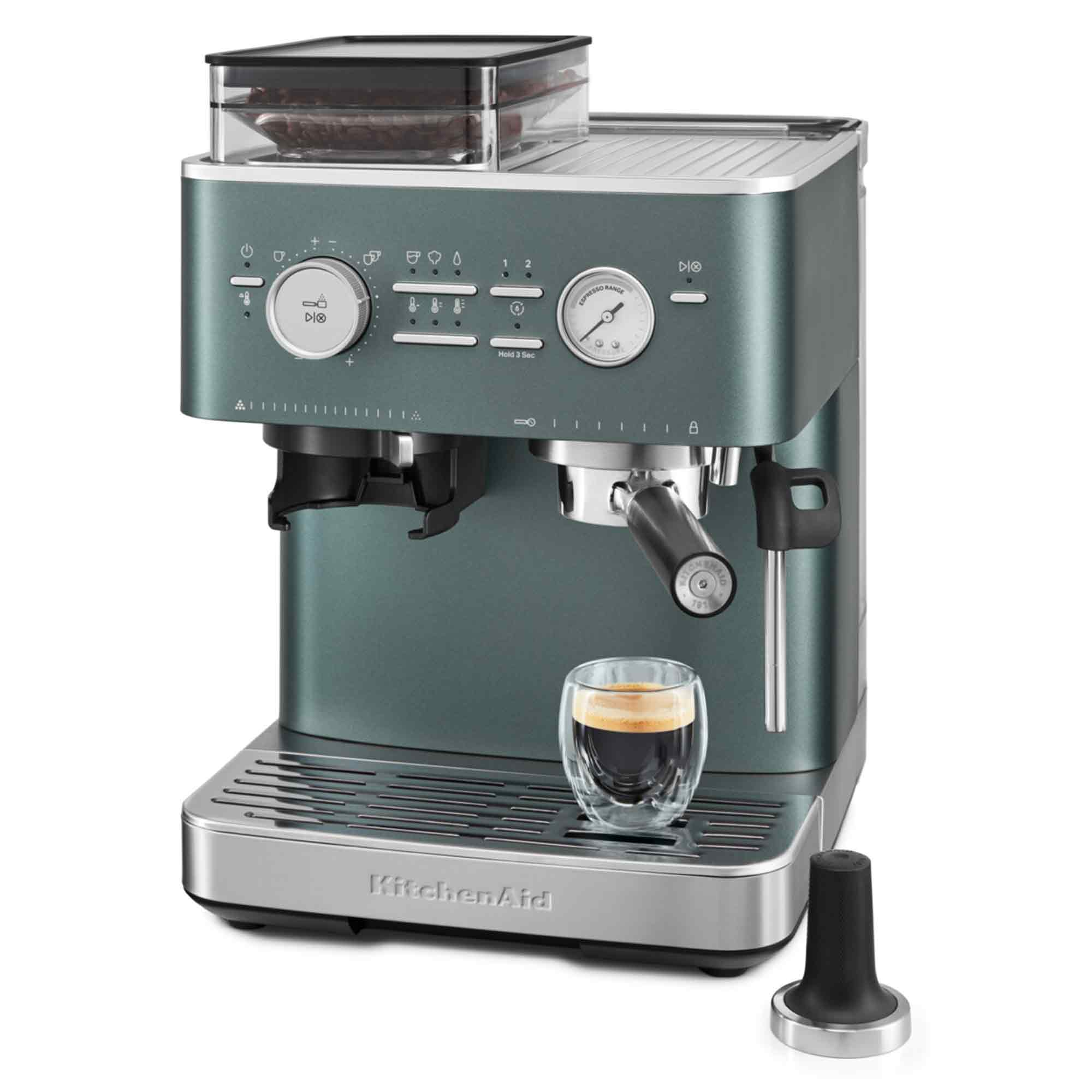 Eine türkisfarbene KitchenAid-Espressomaschine mit einem Glas Espresso. Ein Tamper befindet sich rechts. Kaffeebohnen sind im Behälter.
