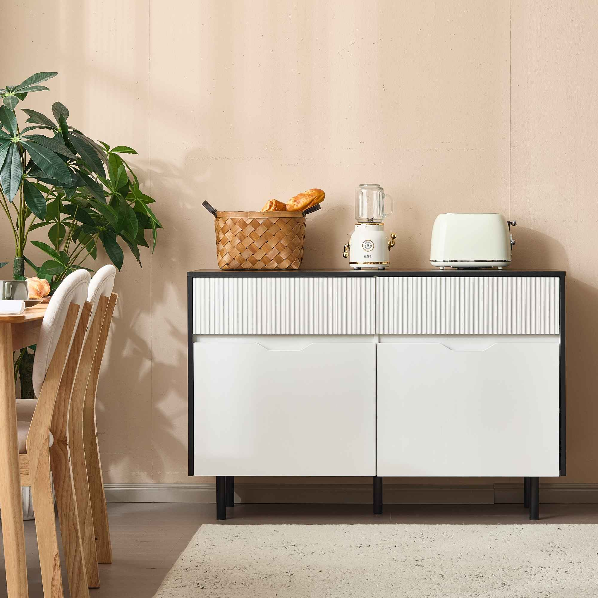 Ein Raum mit einem weißen Schrank, einem Mixer, einem Toaster und einem Korb mit Brot, neben einem Tisch und einer Pflanze.