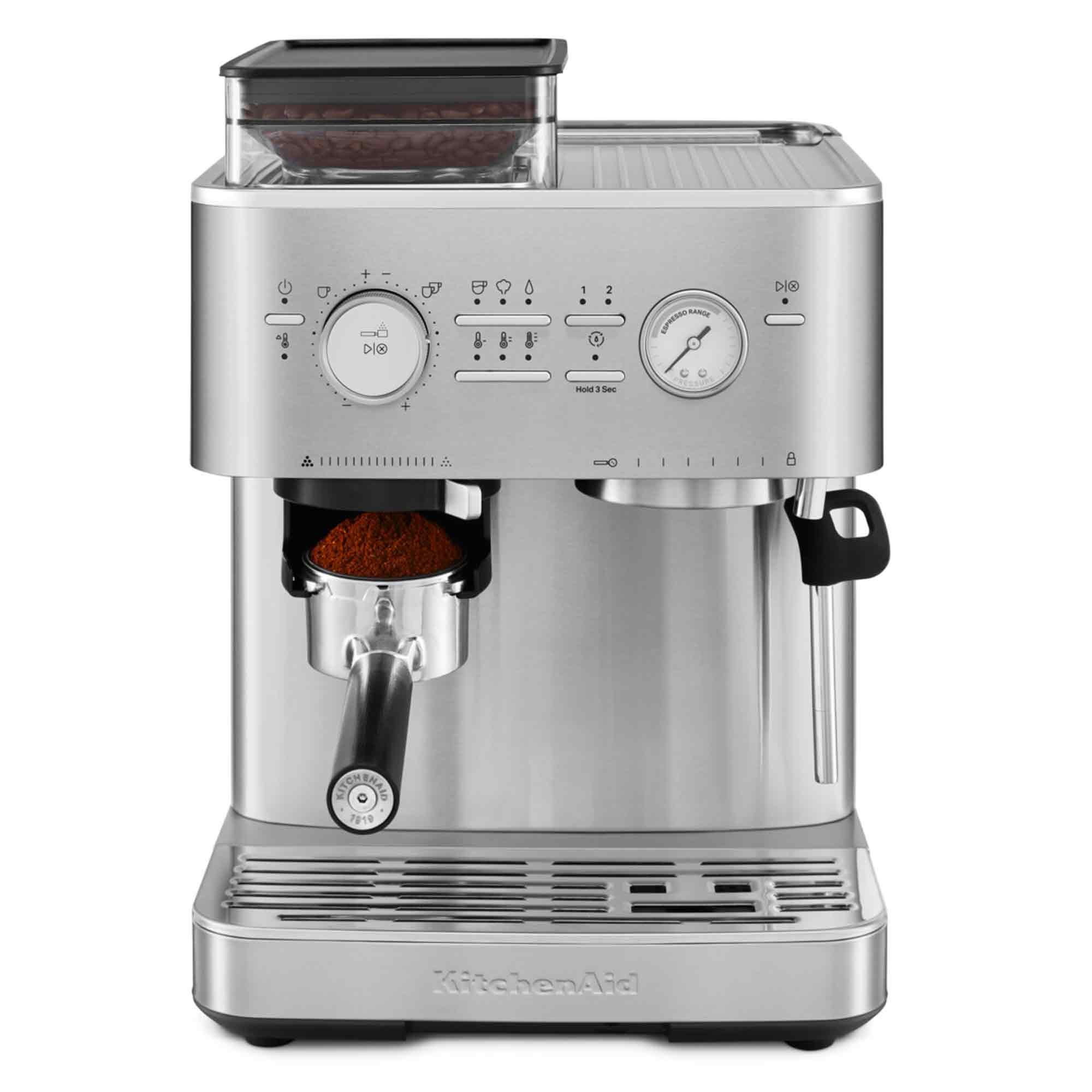 Eine silberne KitchenAid Espressomaschine. Sie hat einen Bohnenbehälter, Drehregler, ein Manometer und einen mit Kaffeepulver gefüllten Siebträger.