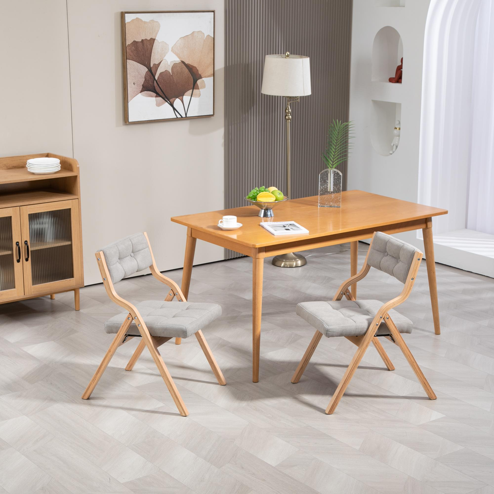 Ein Esszimmer mit Holztisch, zwei grauen Stühlen, einem Schrank und einem Gemälde. Lampe, Obstschale auf dem Tisch.