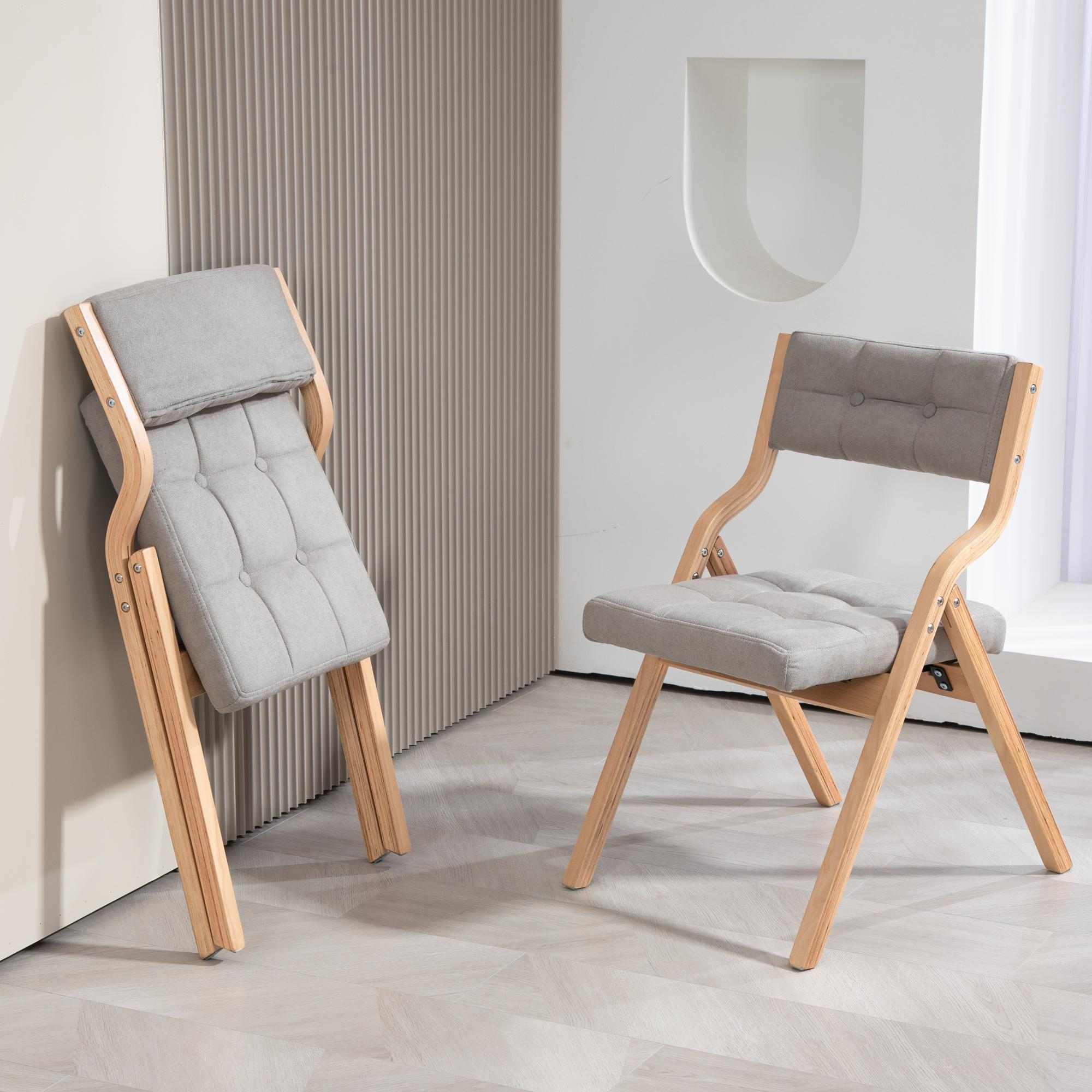 Zwei Klappstühle mit grau gepolsterten Sitzen und Holzrahmen. Einer ist an einer Wand zusammengeklappt. Der andere ist offen.