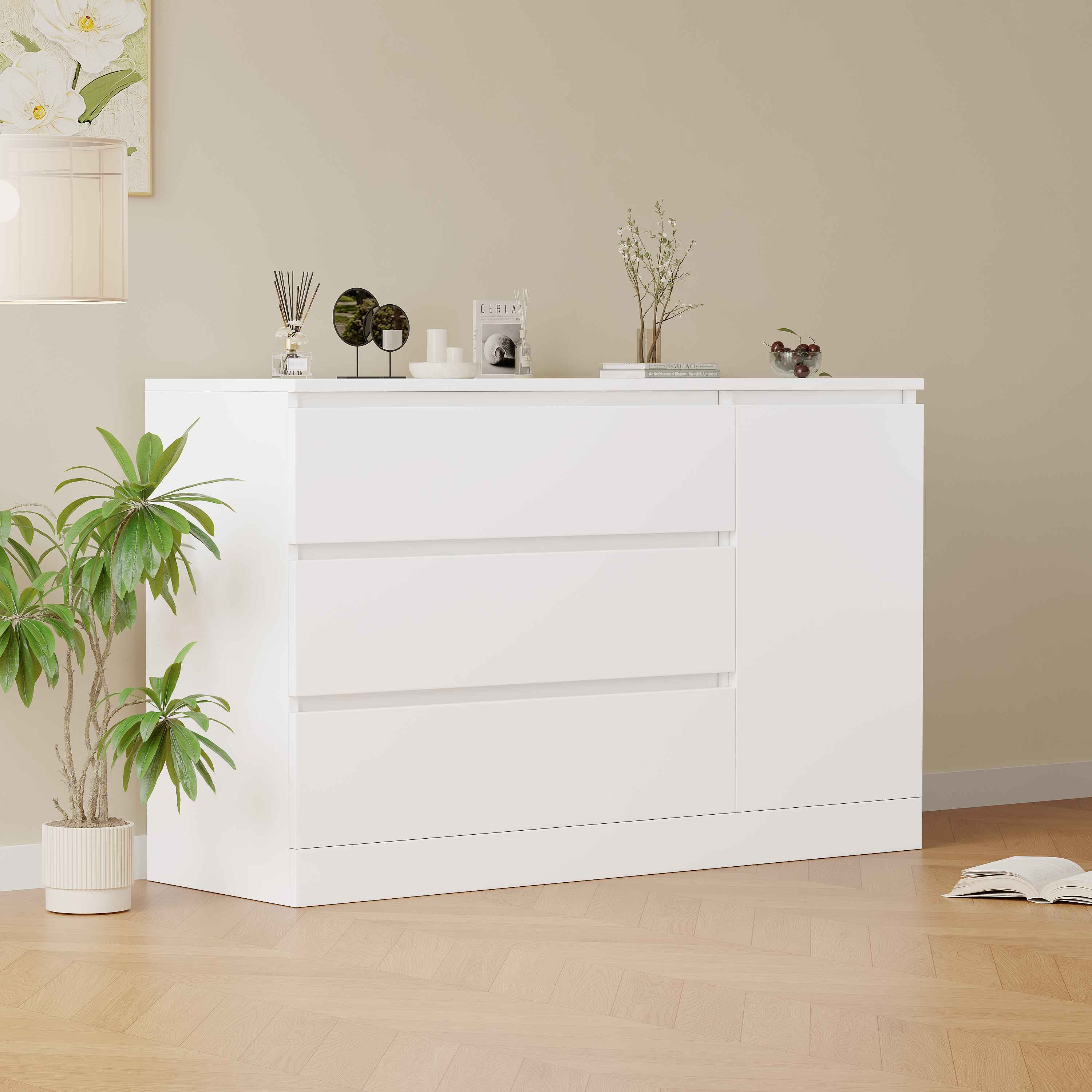 Ein weißer Schrank mit drei Schubladen und einer Tür. Er hat Dekorationen, eine Pflanze und ein Buch. Die Wand ist beige.