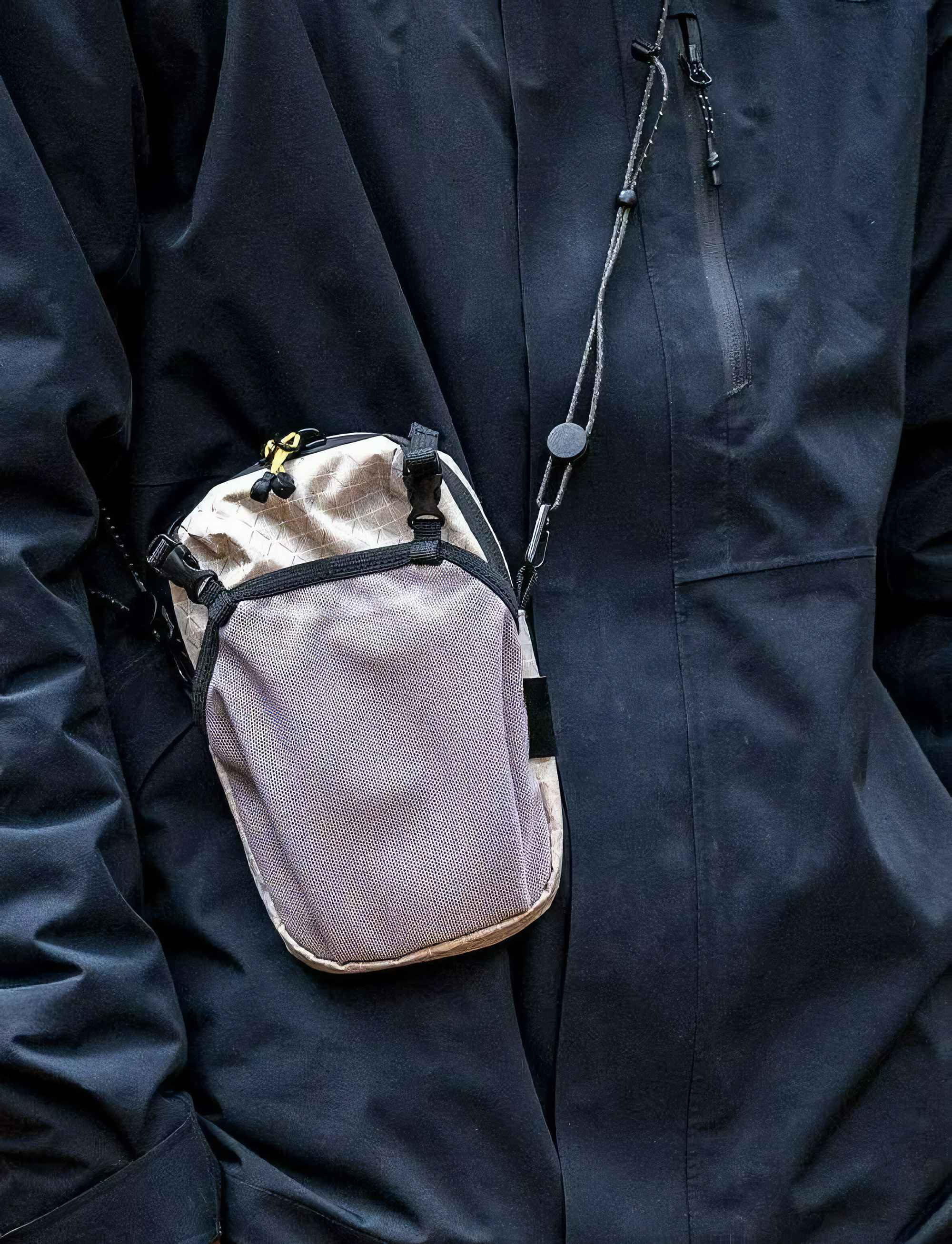 Eine Person mit schwarzer Jacke hat eine beige Tasche über der Brust hängen. Die Tasche hat einen schwarzen Riemen.