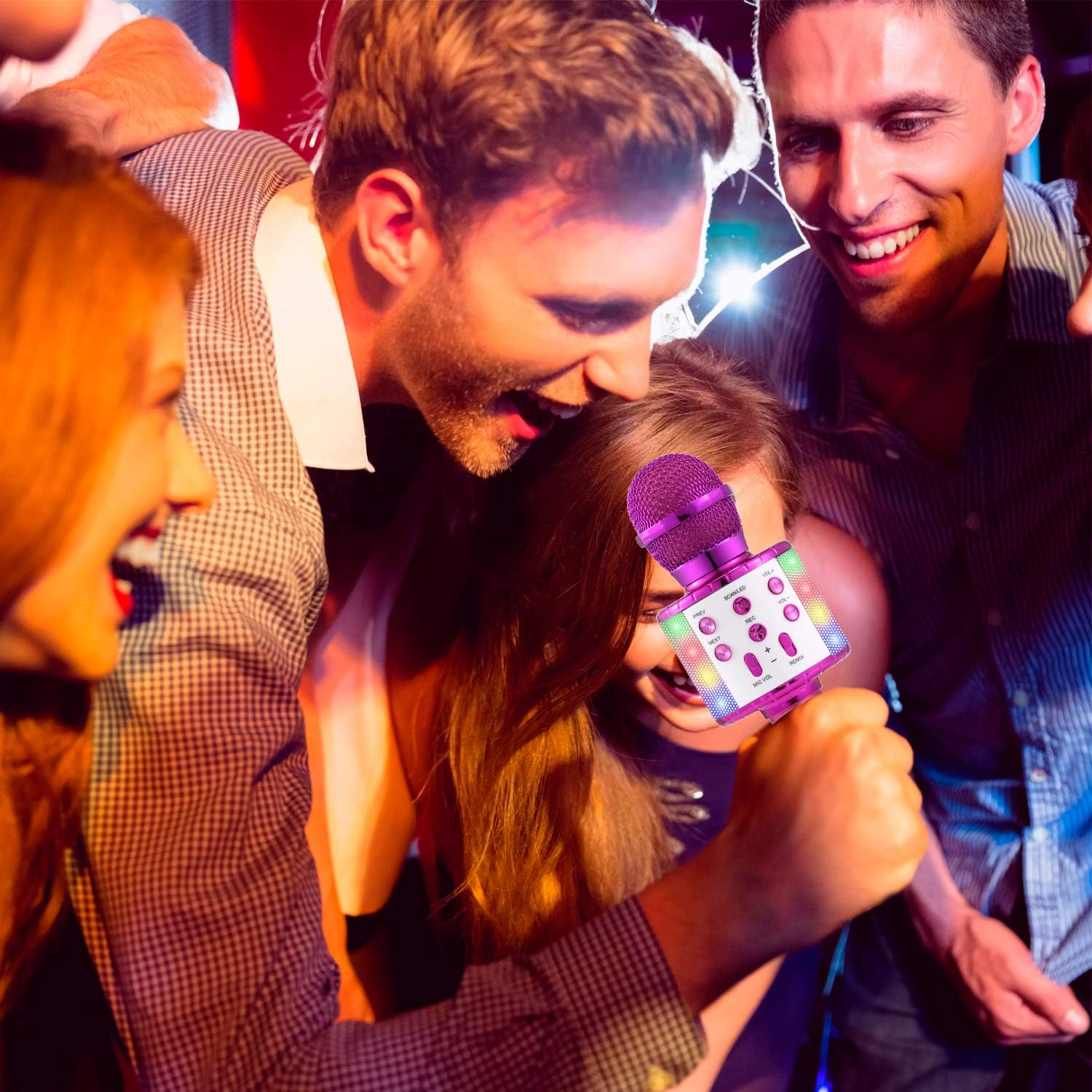 Eine Gruppe von Freunden singt Karaoke. Ein lila Mikrofon wird hochgehalten, umgeben von lächelnden Gesichtern in dunkler Umgebung.