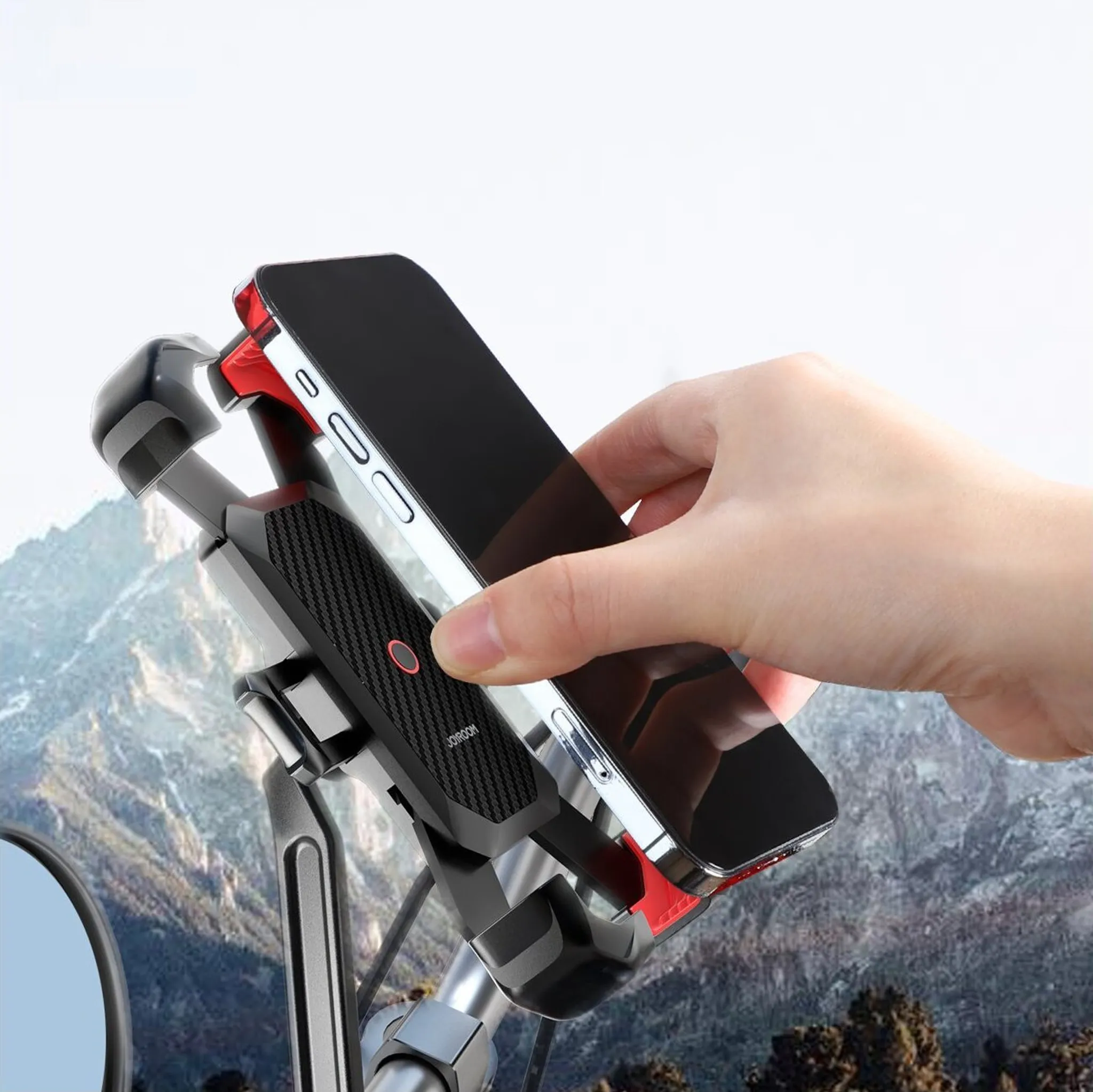 Eine Hand hält ein Smartphone in einer an einem Fahrrad befestigten Telefonhalterung. Der Hintergrund zeigt Berge.
