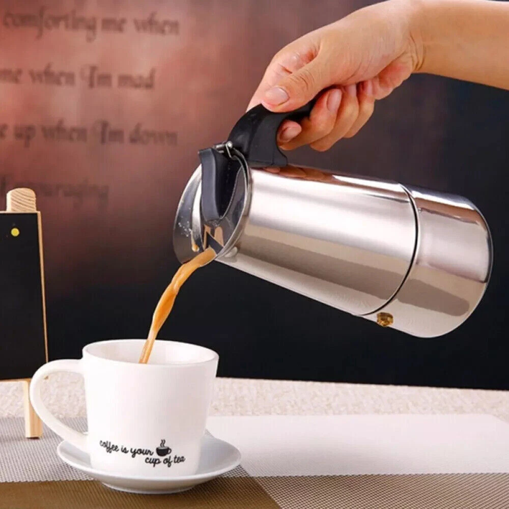 Eine Hand gießt Kaffee aus einer silbernen Kanne in eine weiße Tasse auf einer Untertasse. Auf der Tasse steht 'coffee is your cup of tea'.
