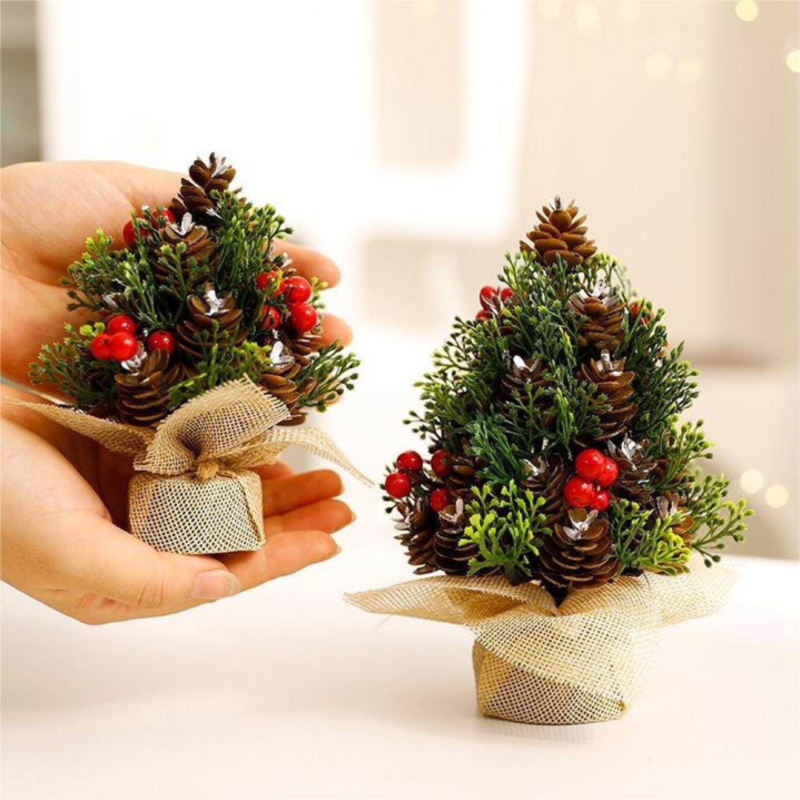 Zwei Miniatur-Weihnachtsbäume. Jeder hat Tannenzapfen, rote Beeren und ist in Jute verpackt. Einer wird in Händen gehalten.