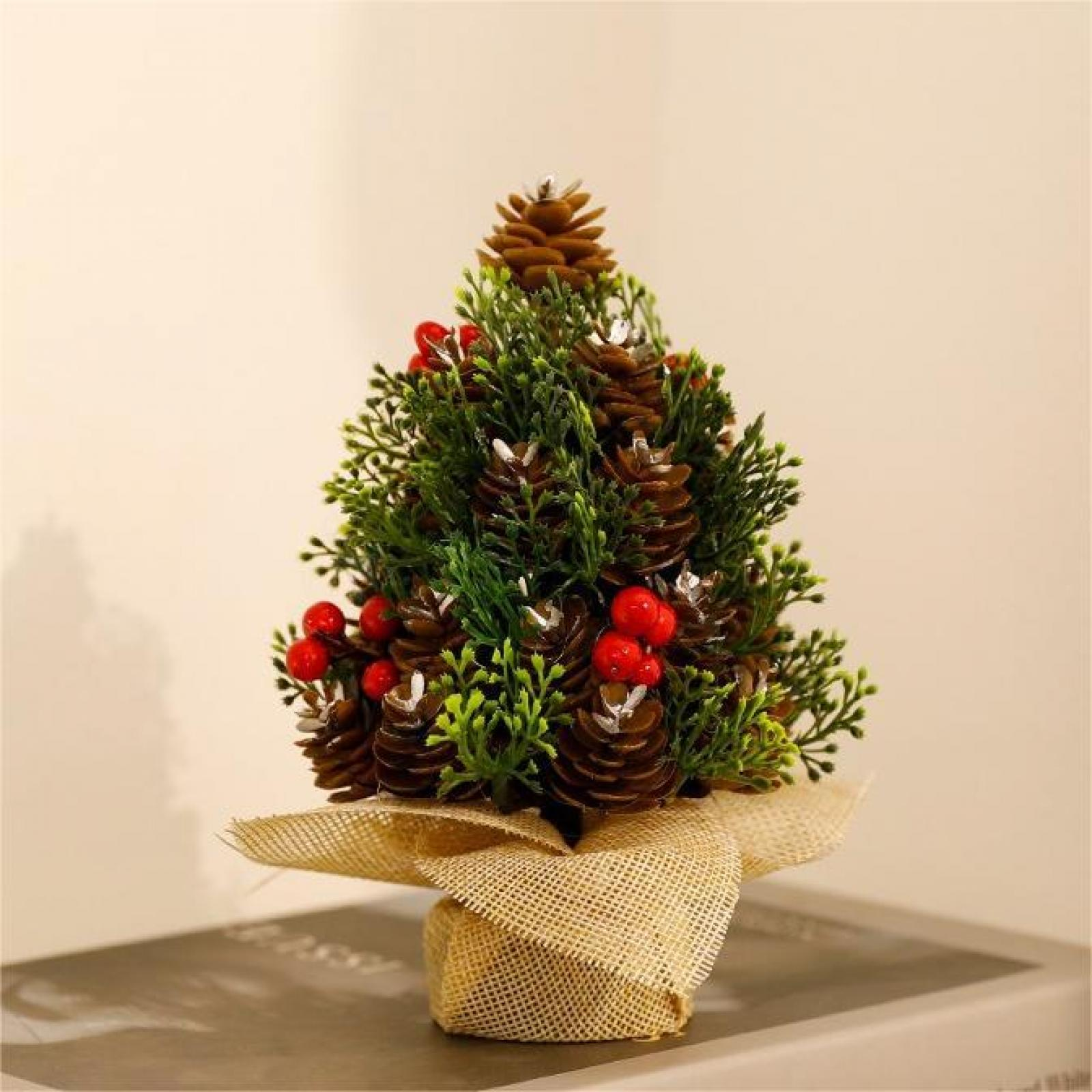 Miniatur-Weihnachtsbaum. Er hat Tannenzapfen, rote Beeren und grünes Laub auf einem mit Sackleinen umwickelten Sockel. Hellbeiger Hintergrund.