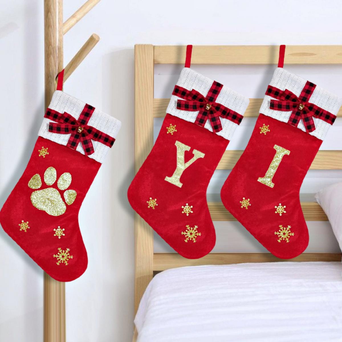 Drei rote Weihnachtsstrümpfe mit weißen Oberteilen, schwarzen Karobögen, goldenen Buchstaben und Schneeflocken. Einer hat einen Pfotenabdruck.