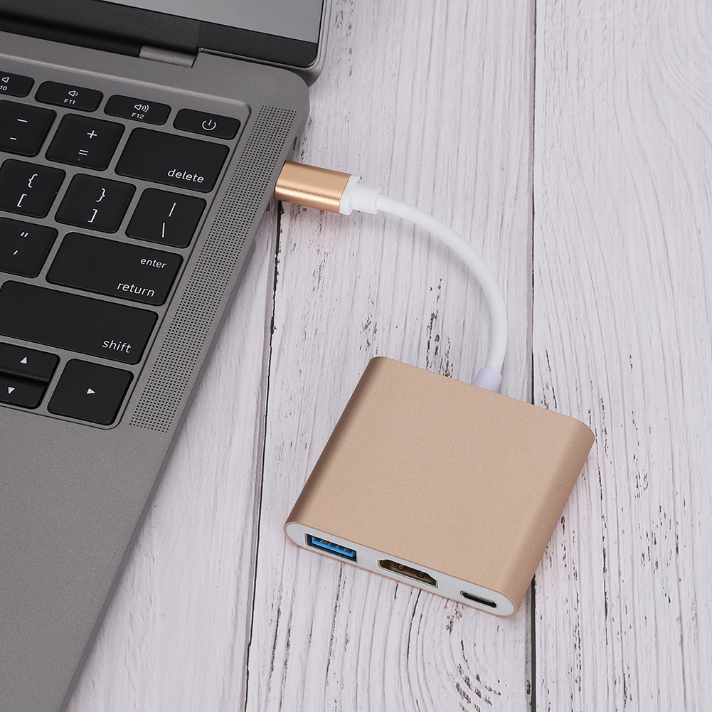 Ein Laptop, der über ein weißes Kabel mit einem goldenen Adapter verbunden ist. Der Adapter befindet sich auf einer Holzoberfläche. Tastatur sichtbar.