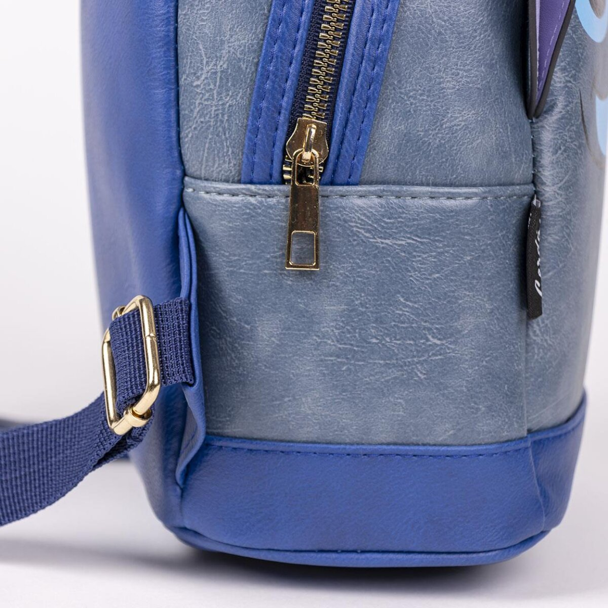 Primer plano de una mochila azul con cremallera y detalles de correa dorados. La bolsa tiene tonos azules claros y oscuros.