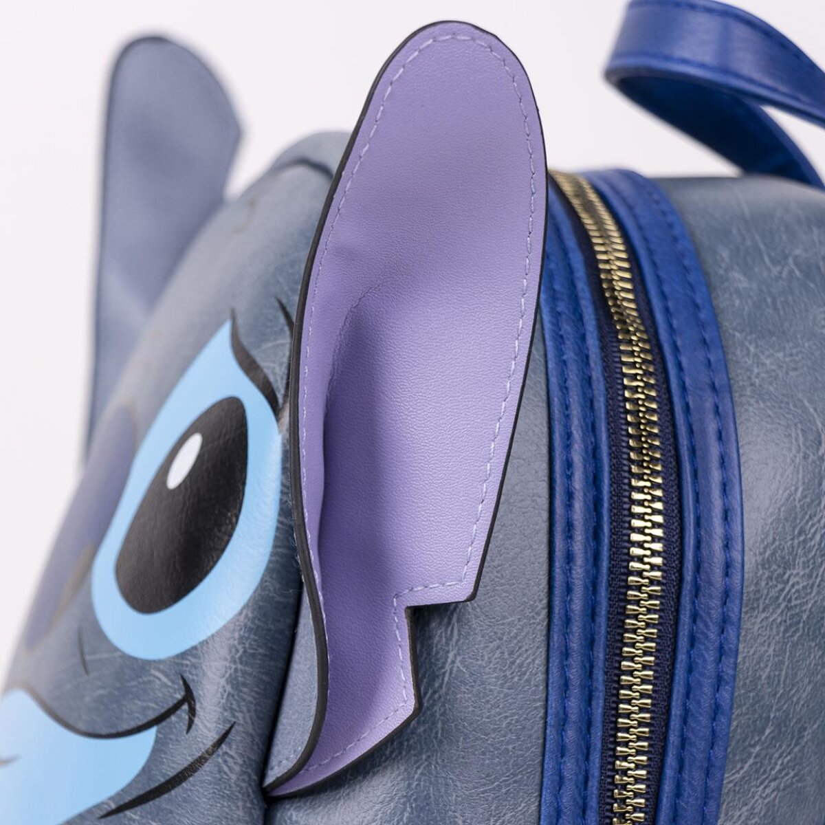Primer plano de una mochila con tema de Stitch. Presenta una combinación de colores azul y morado, con una oreja prominente y detalles de cremallera.