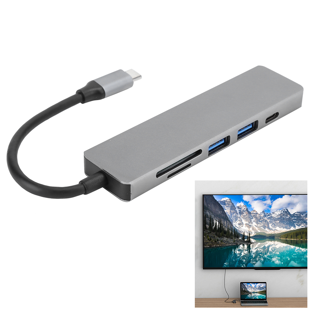 Ein silberner USB-C-Hub mit mehreren Anschlüssen ist mit einem Laptop und einem Fernseher verbunden, der eine Landschaft zeigt.