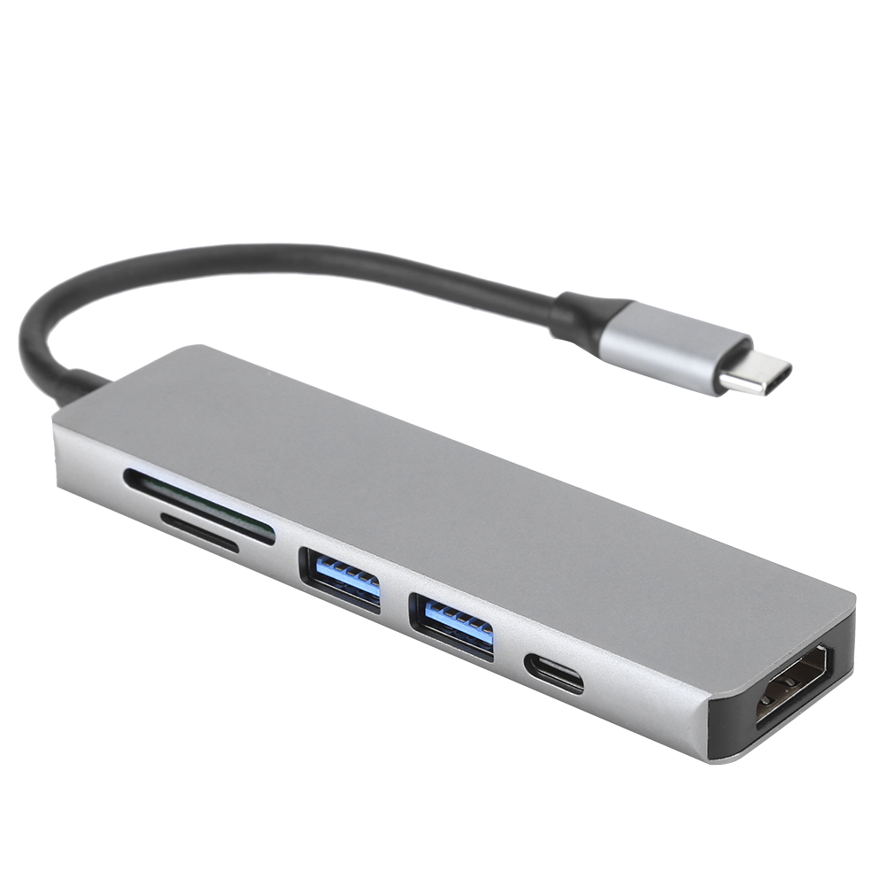 Ein silberner USB-C-Hub mit mehreren Anschlüssen, darunter USB, HDMI und SD-Kartenleser. Ein schwarzes Kabel verbindet sich mit einem USB-C-Anschluss.