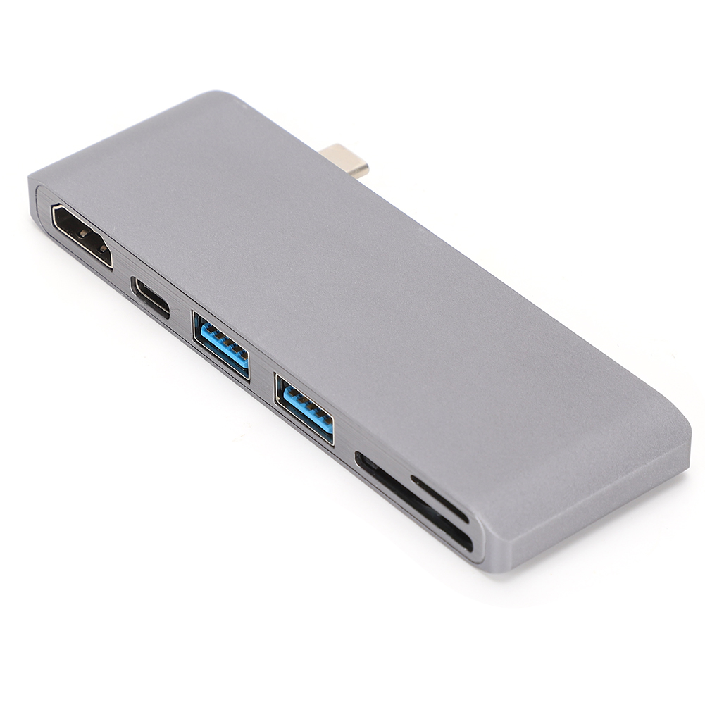 Ein silberner USB-C-Hub mit mehreren Anschlüssen, einschließlich HDMI, USB 3.0 und SD-Kartenleser, liegt auf einer weißen Oberfläche.