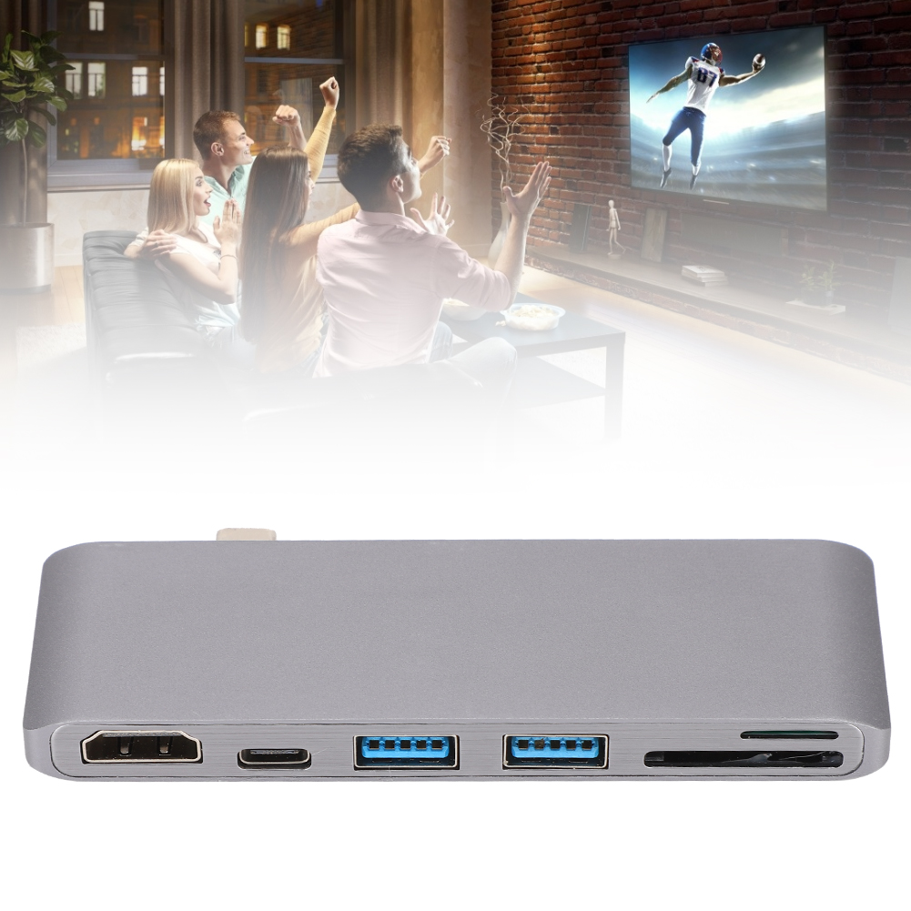 Leute schauen fern, jubeln. Vordergrund: grauer Hub mit HDMI, USB-Anschlüssen. Hintergrund: Footballspiel im Fernsehen, Backsteinmauer.