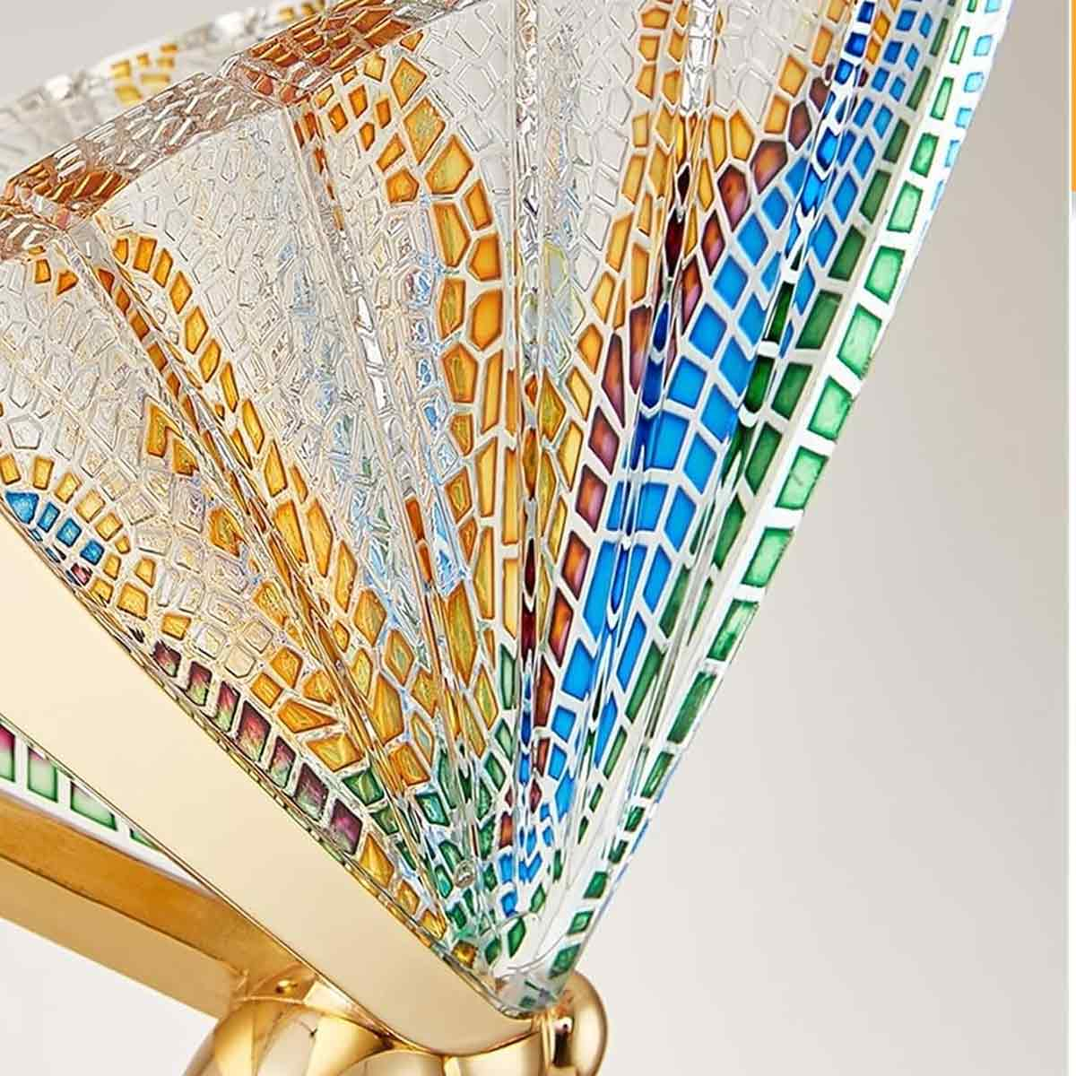 Nahaufnahme eines bunten Glasfächers. Er hat gelbe, orange, blaue und grüne Mosaikmuster und einen goldenen Sockel.