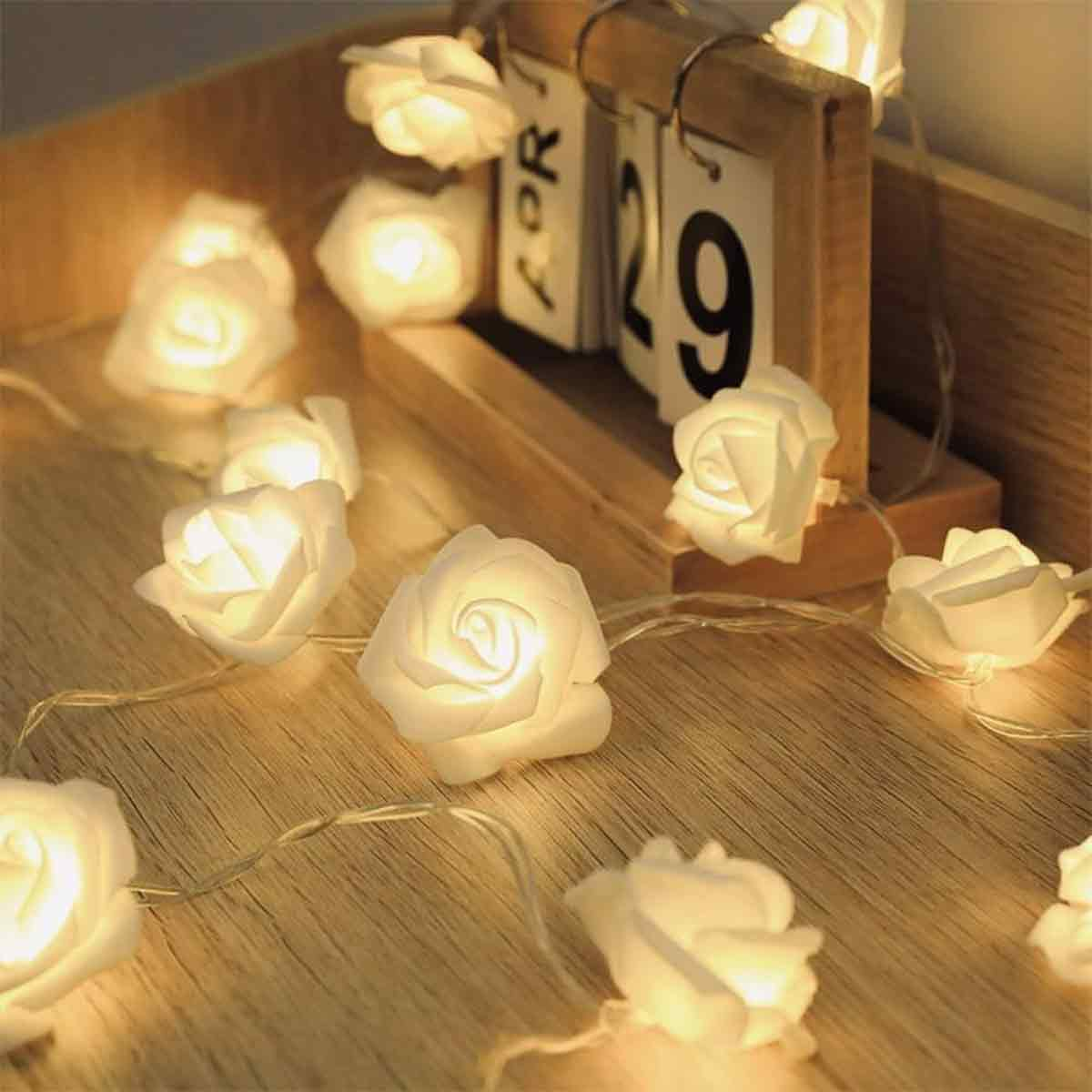 Lichterkette mit weißen rosenförmigen Lichtern auf einer Holzoberfläche. Ein Holzkalender zeigt die Zahl 29.