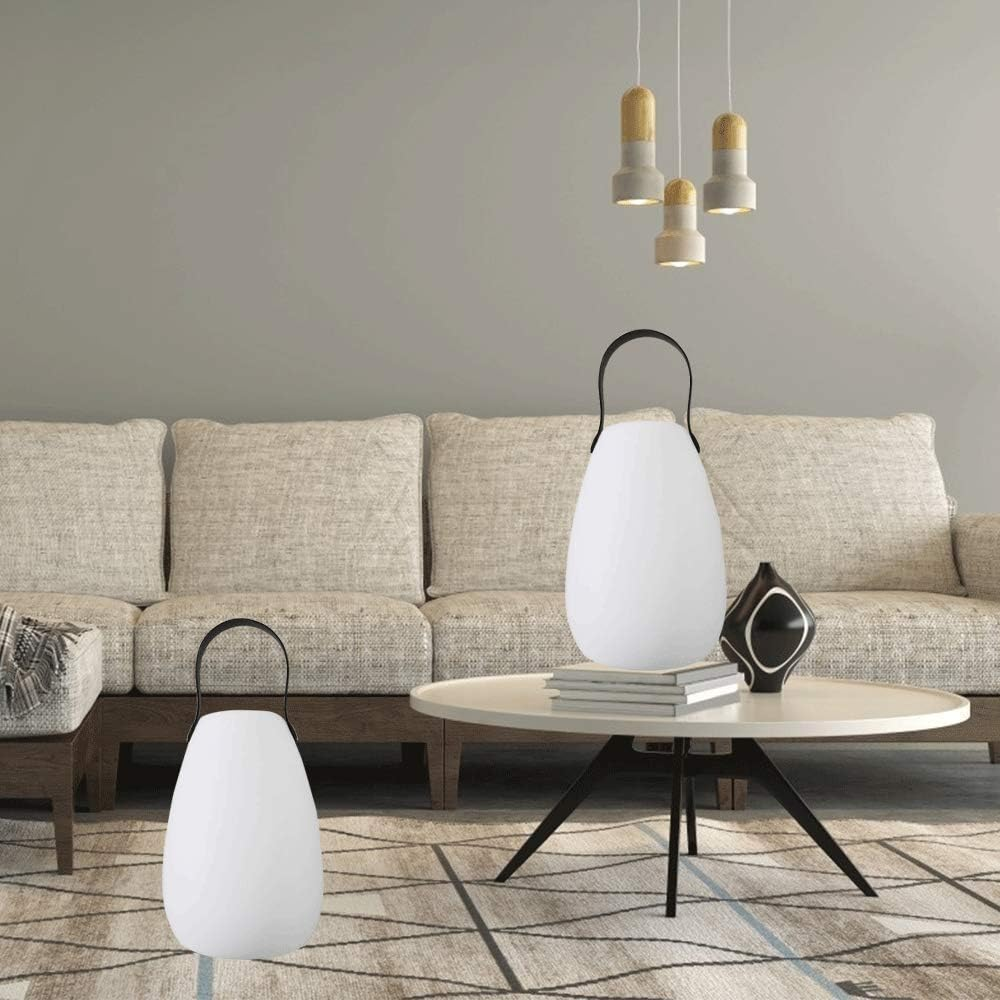 Ein Wohnzimmer mit einer weißen Lampe mit schwarzem Griff, einem Sofa, einem Tisch und Pendelleuchten von der Decke.