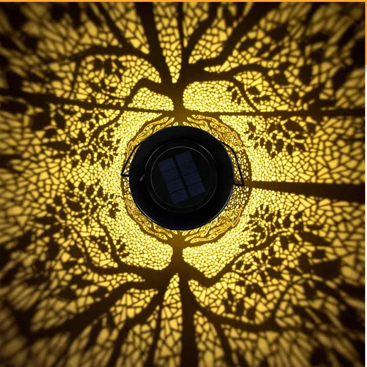 Eine Solarlampe wirft einen baumartigen Schatten auf eine Oberfläche. Die Lampe ist schwarz mit einem Solarpanel. Das Licht ist gelb.