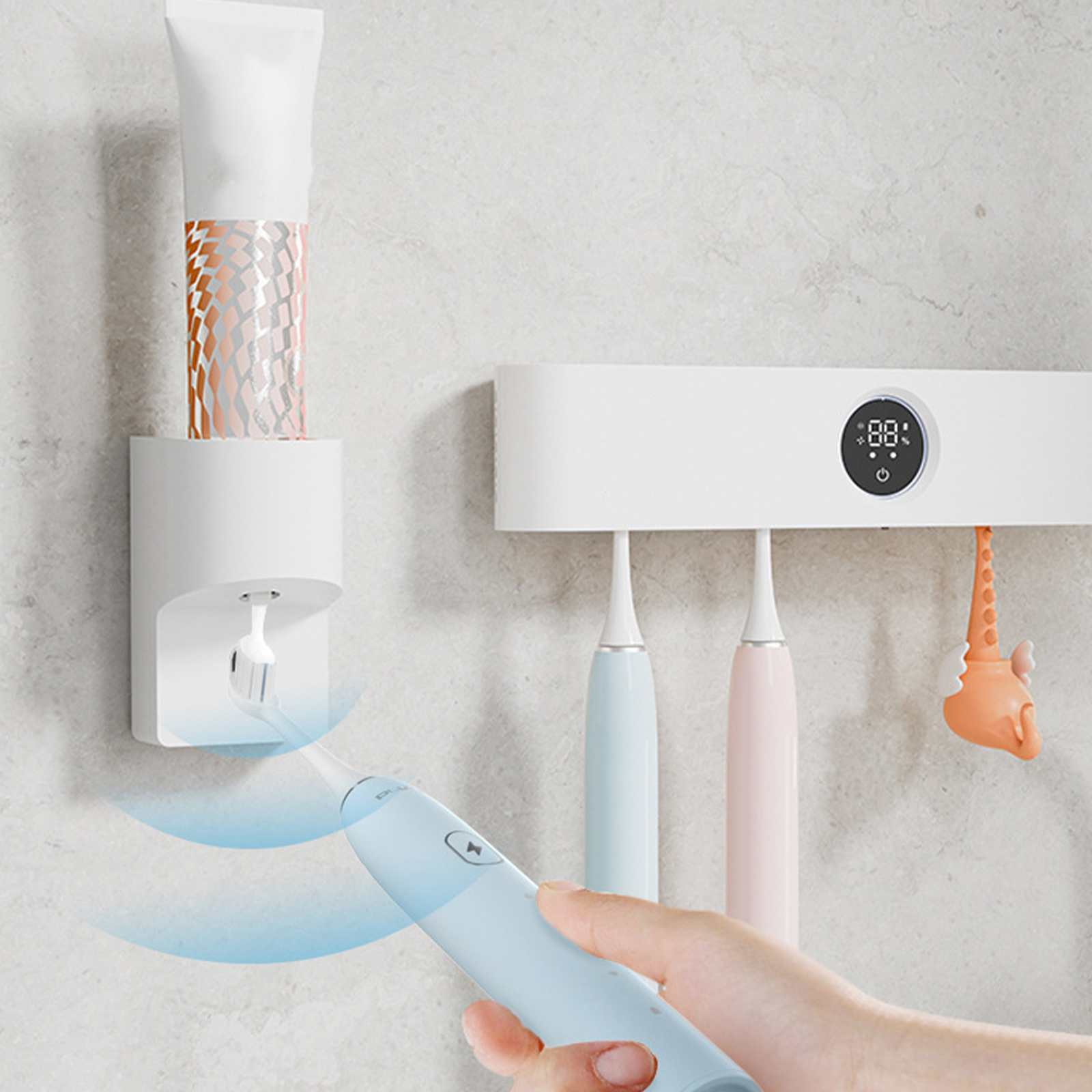 Ein an der Wand befestigter Zahnbürstenhalter mit einem Zahnpender und drei elektrischen Zahnbürsten. Hand, die eine blaue Zahnbürste hält.