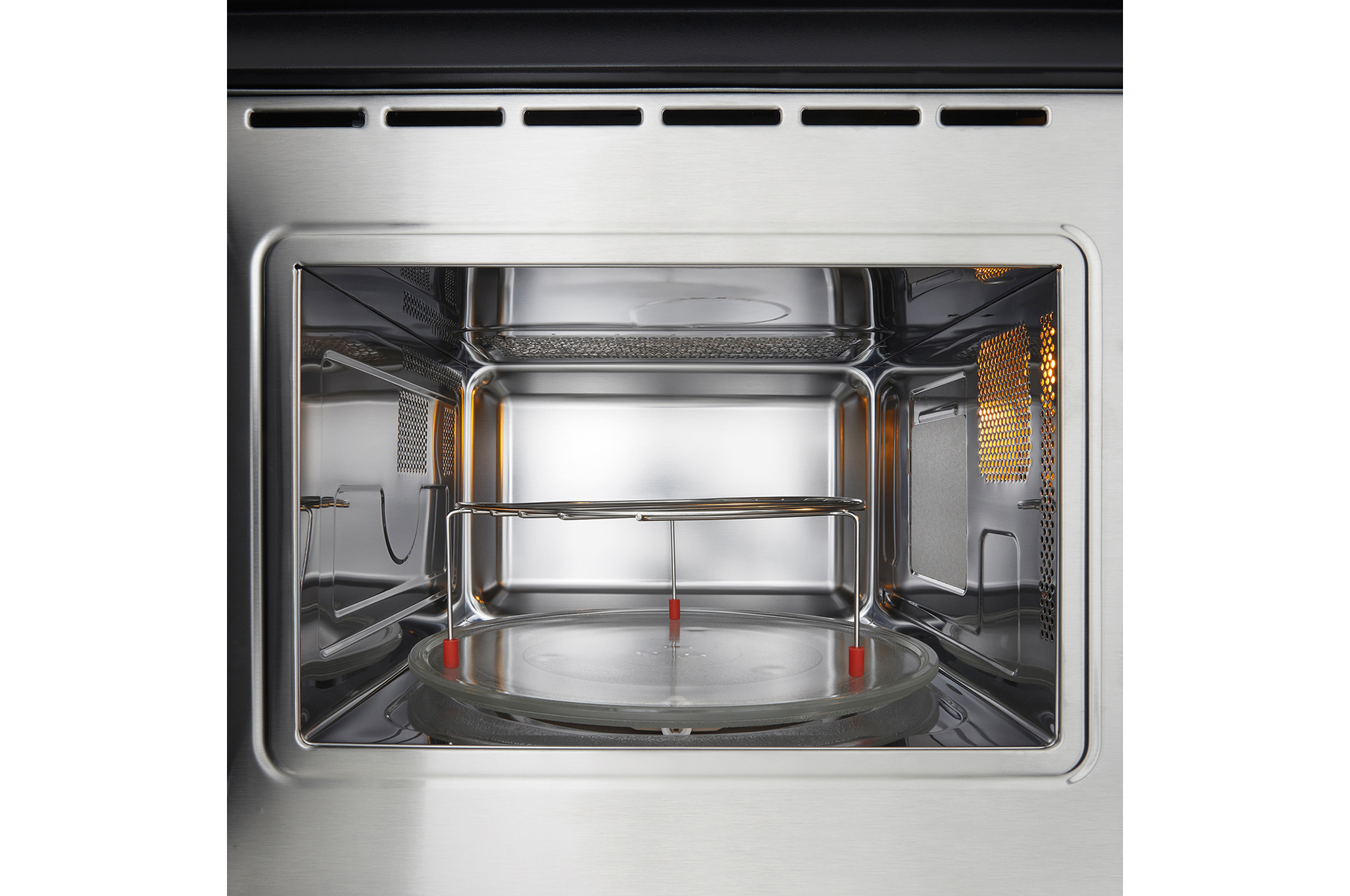 Dentro de un horno microondas. Se ve una placa de vidrio y una rejilla metálica. El horno es de acero inoxidable y tiene el interior iluminado.