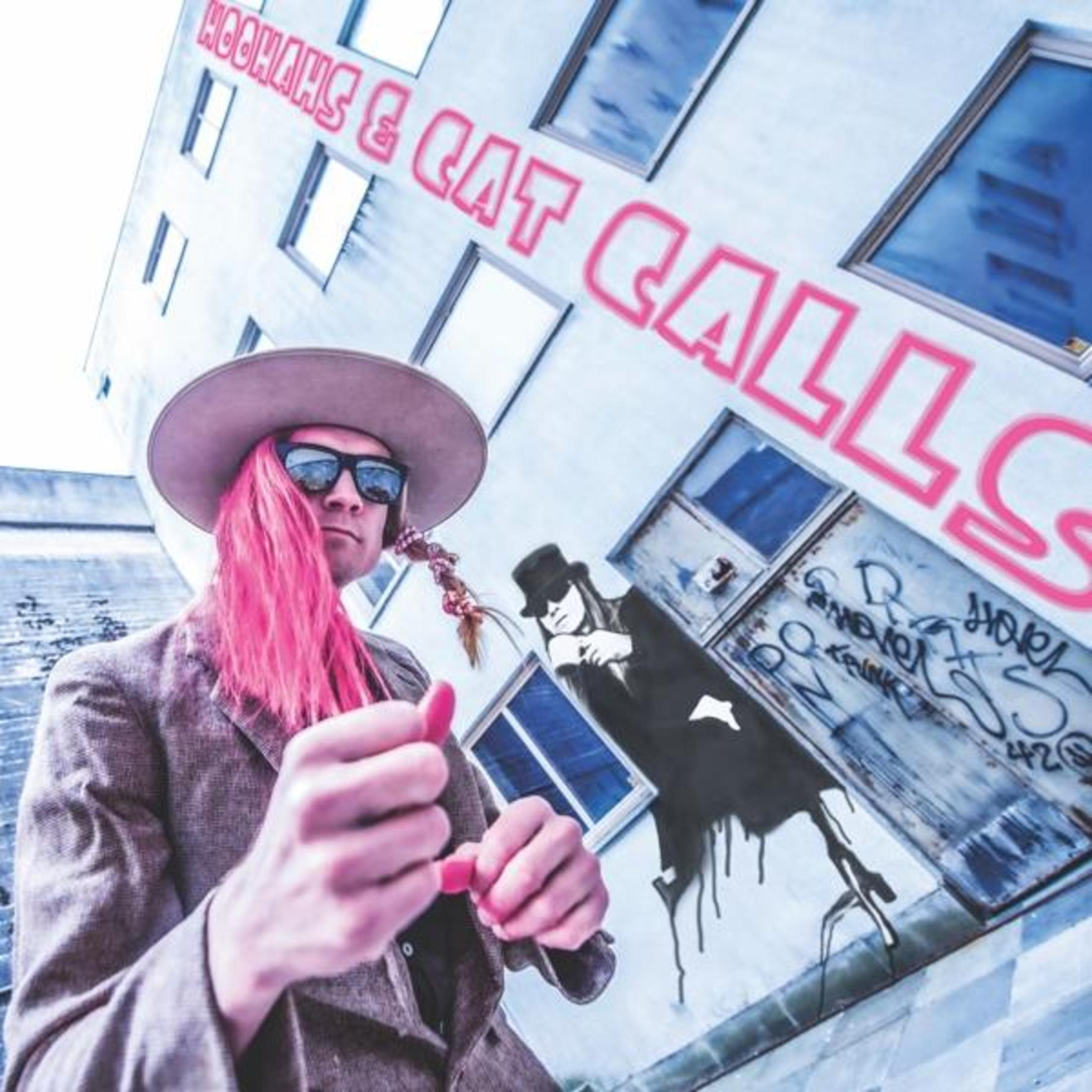 Mann mit pinkfarbenem Haar und Sonnenbrille, trägt Hut und Blazer, vor einem Gebäude mit pinkfarbenem Text und Graffiti.
