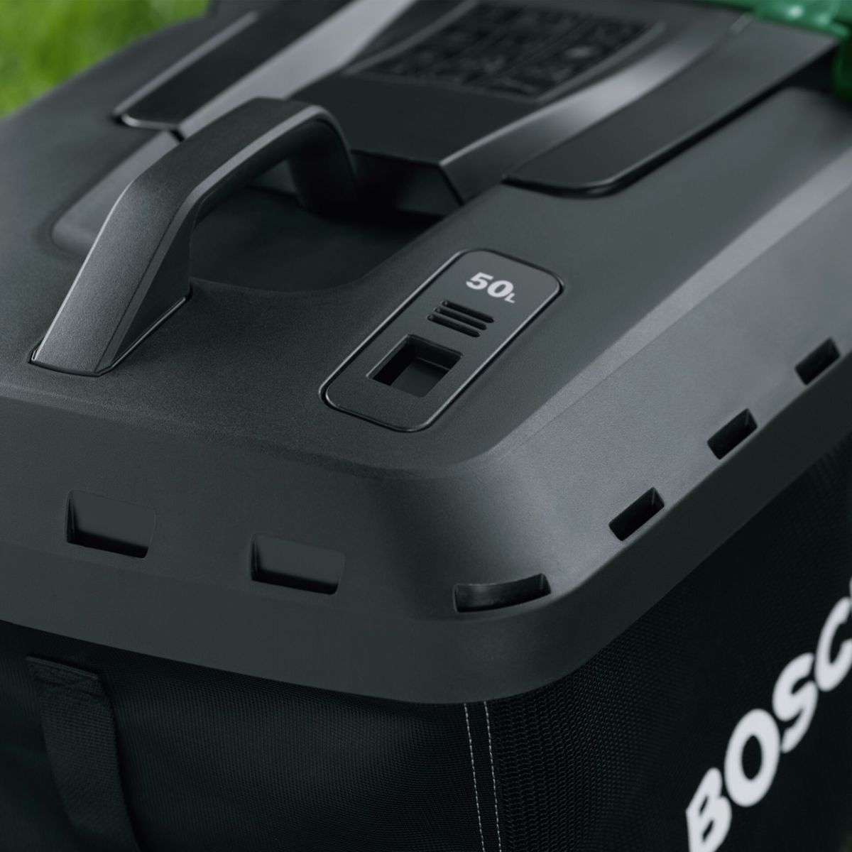 Primer plano de una bolsa negra de cortacésped. Cuenta con un asa, el texto '50L' y el logo BOSCH. Hierba verde en el fondo.