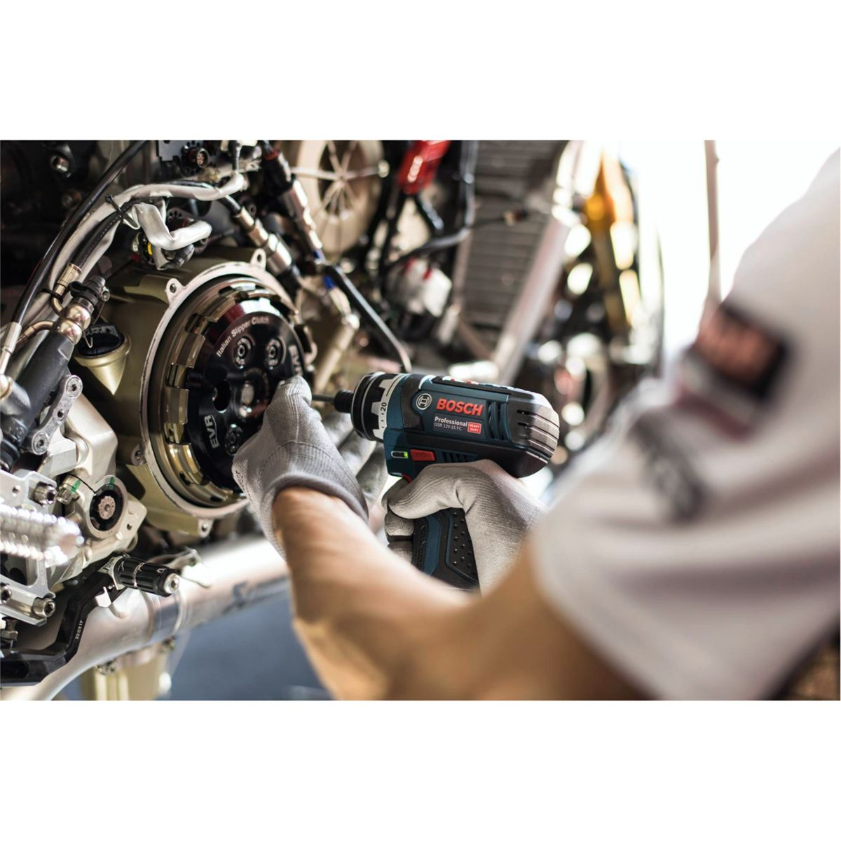 Osoba w rękawicach używa elektronarzędzia Bosch do pracy przy silniku motocykla. Scena ma miejsce w warsztacie.