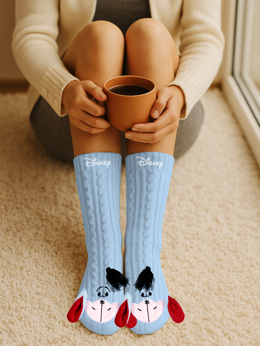 Person sitzt drinnen und hält einen braunen Becher. Sie trägt hellblaue Socken mit Disney-Gesichtern auf einem beigefarbenen Teppich.