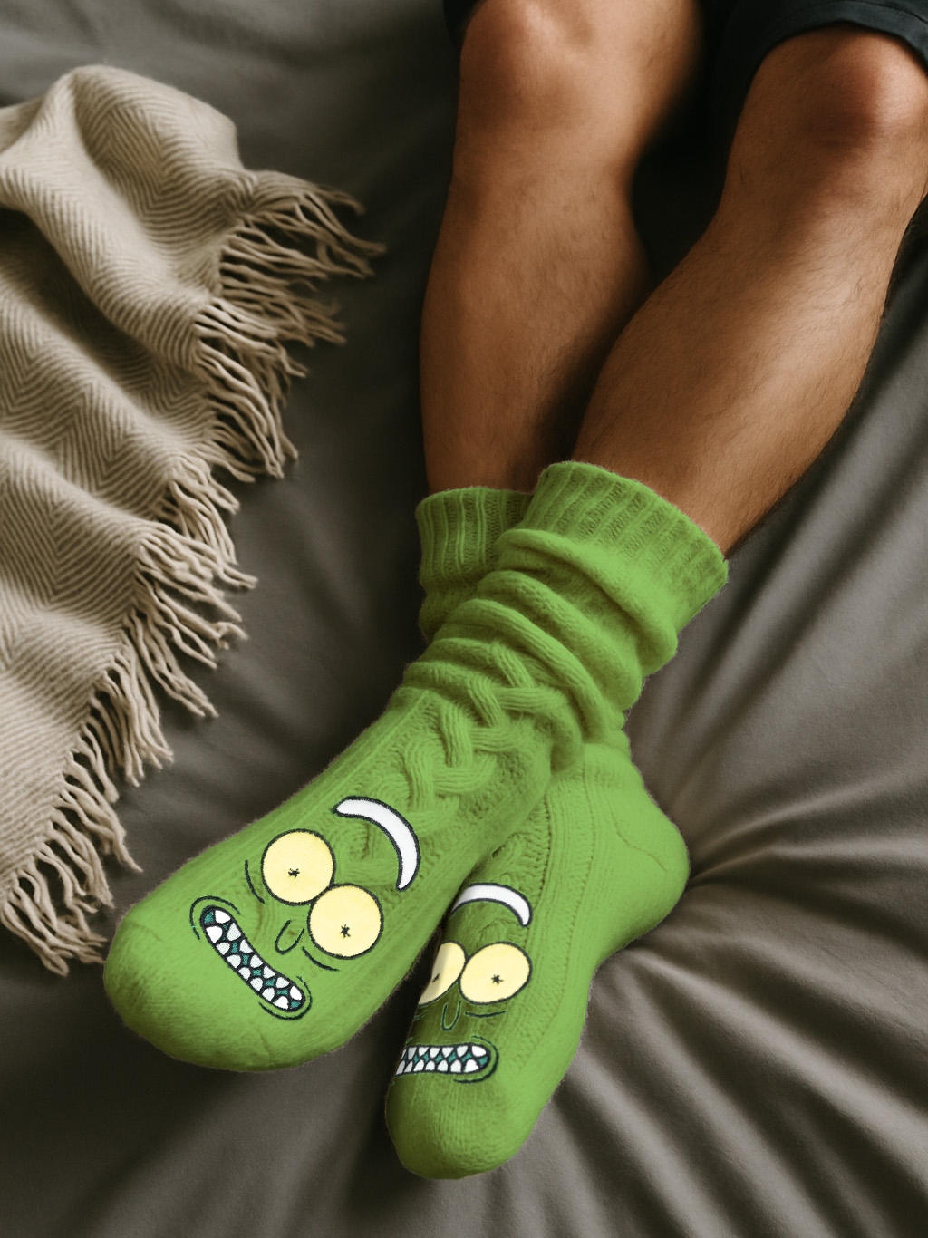 Person trägt grüne Rick-und-Morty-Socken auf einem Bett. Links ist eine Decke. Beine sind sichtbar.