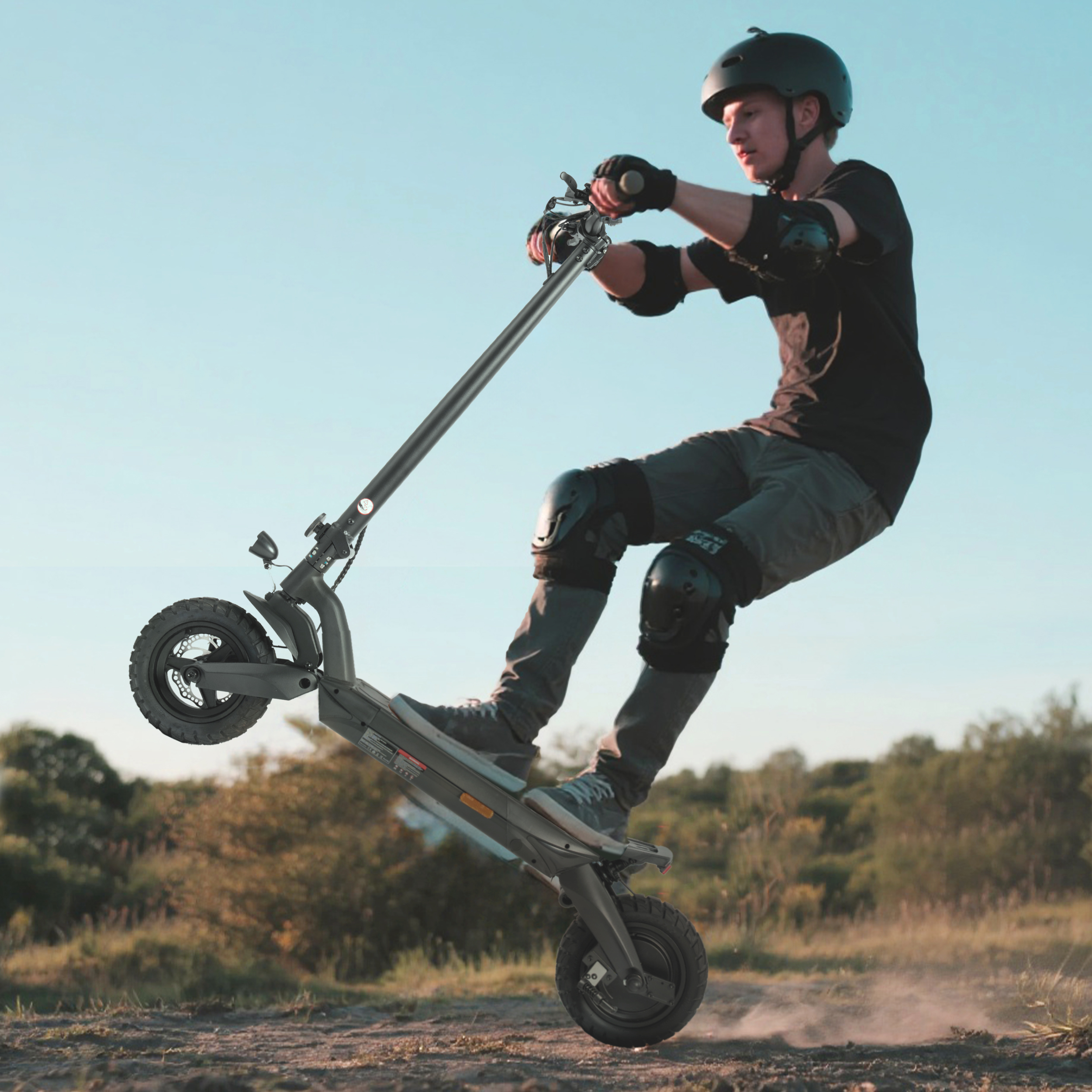 Osoba na hulajnodze elektrycznej robi wheelie. Osoba ma na sobie kask i sprzęt ochronny. Niebo jest niebieskie, a ziemia to ziemia.
