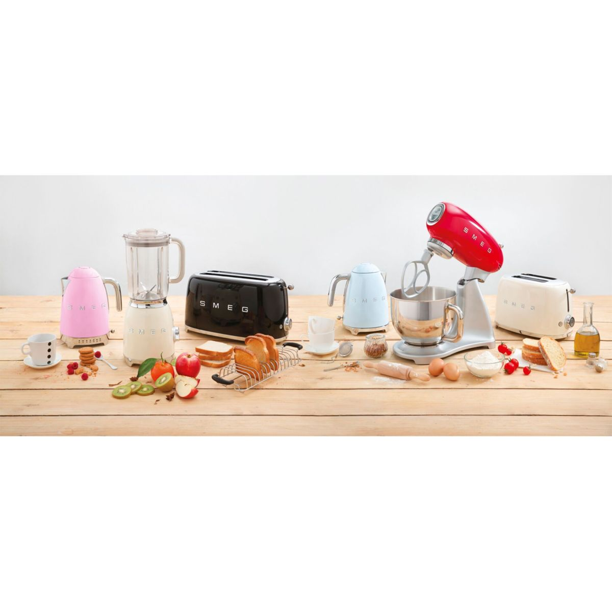 Sprzęt kuchenny na drewnianym stole. Obejmuje różowy czajnik, czarny toster, blender, czerwony mikser i inne składniki do pieczenia.