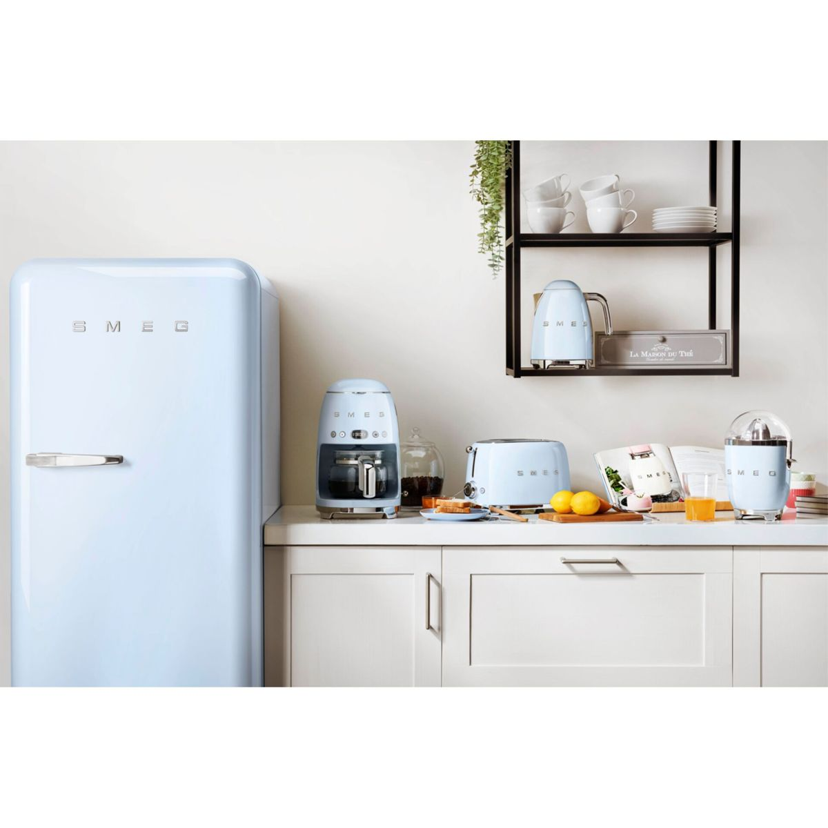 Un set da cucina SMEG azzurro chiaro. Frigorifero, macchina da caffè, tostapane, spremiagrumi e altri accessori su un piano di lavoro bianco.