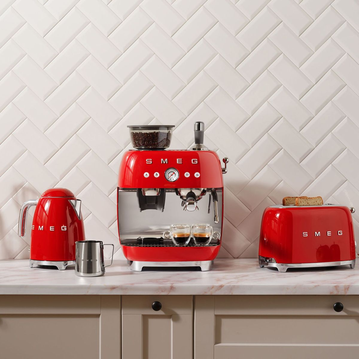 Rode SMEG keukenapparatuur op een marmeren aanrecht: waterkoker, espressomachine met koffie en broodrooster met brood. Witte tegel achtergrond.
